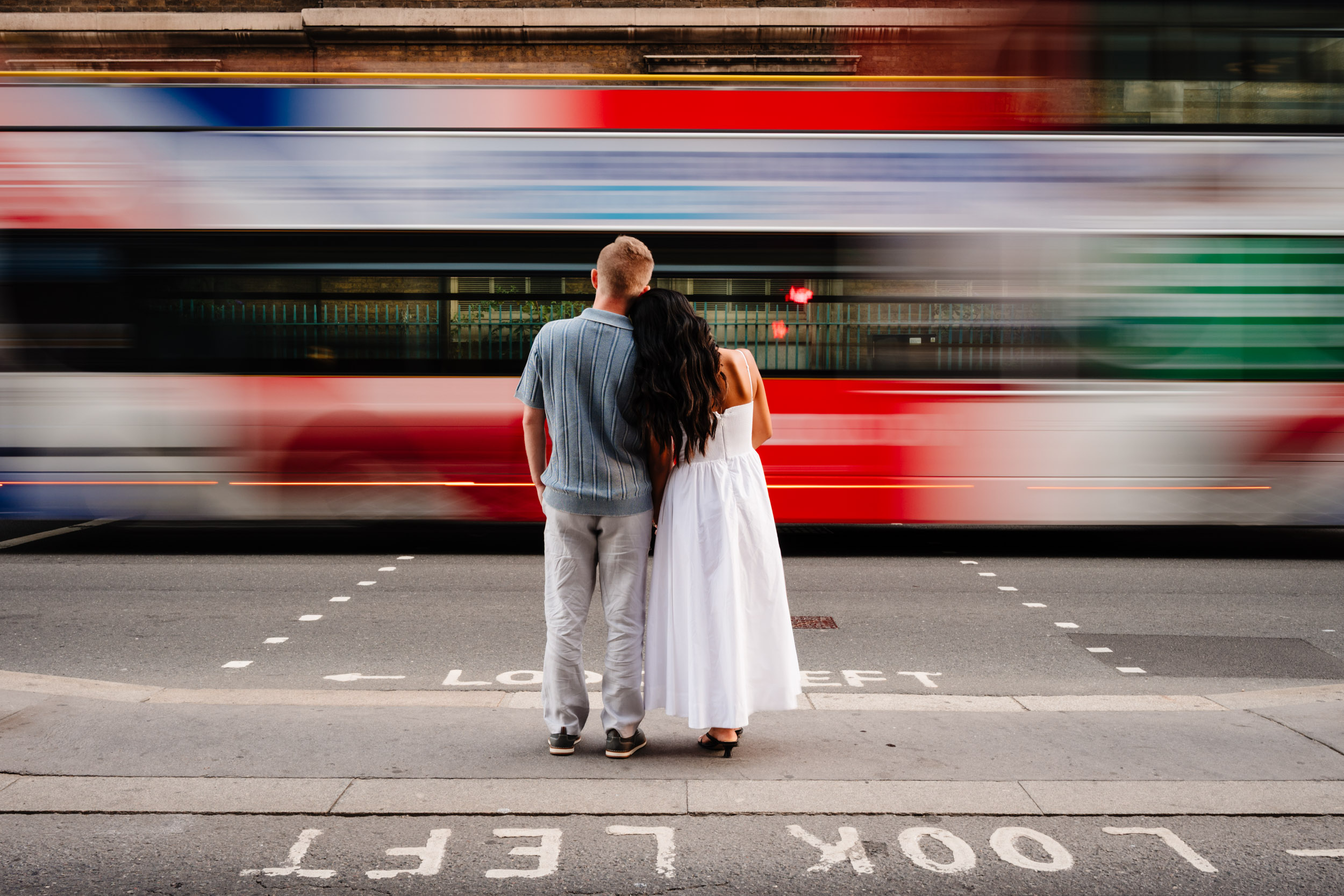 couple waiting at pedestrian crossing bus passes in front of them