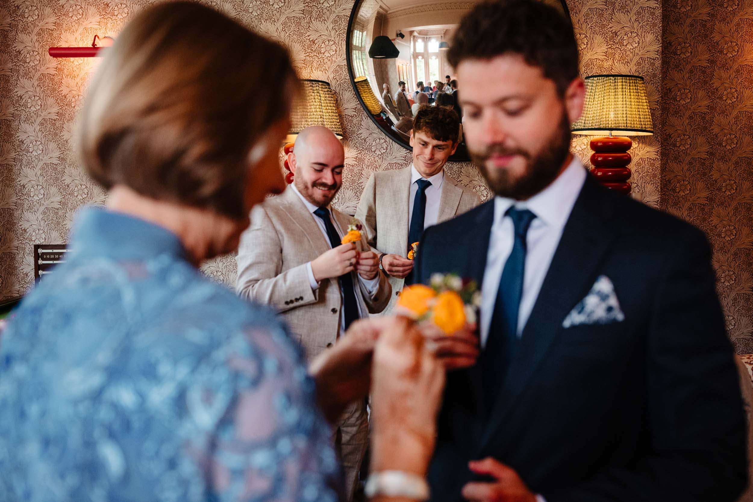 Sam’s mum pinning a flower onto best man Ben’s suit with others helping in the background