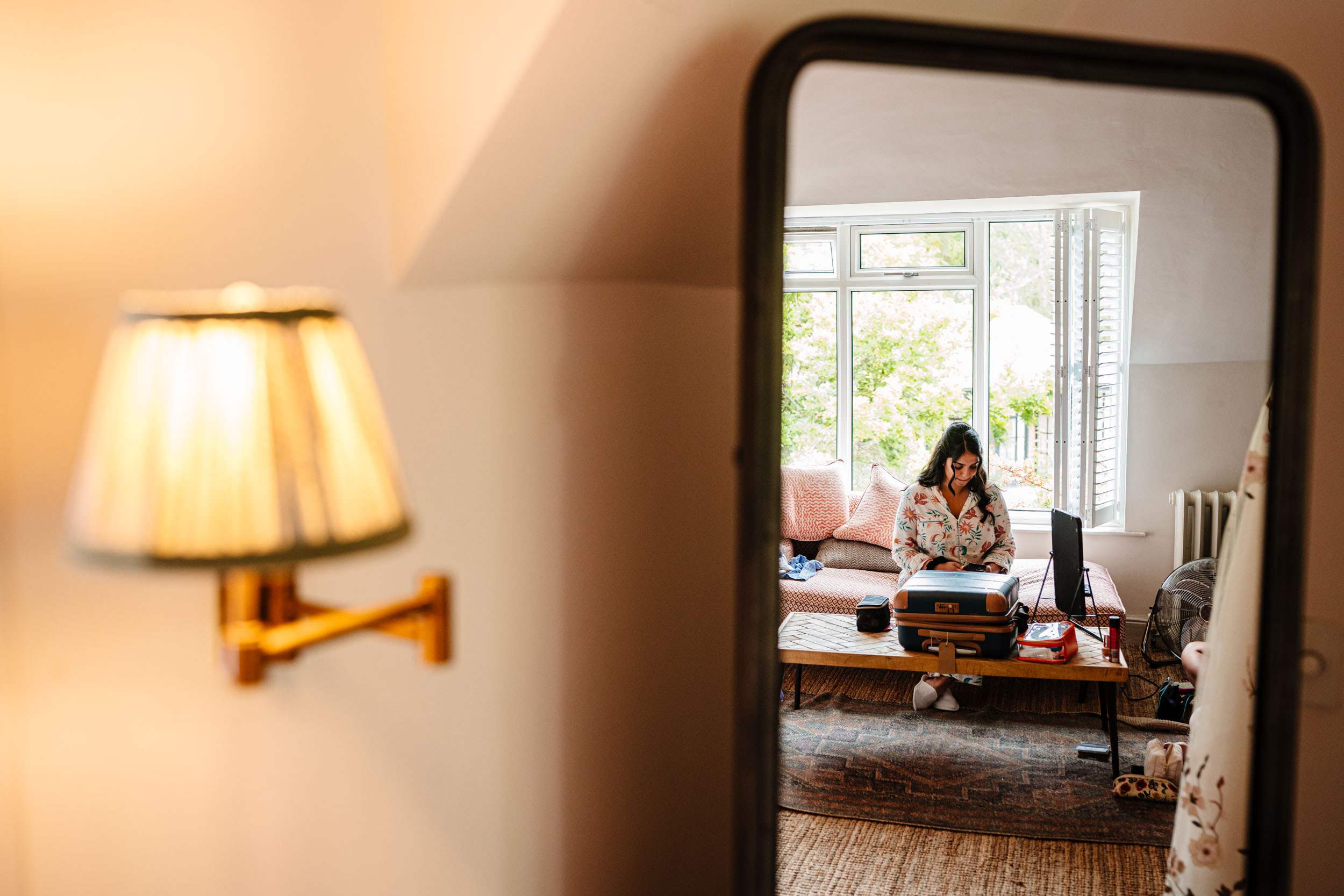 Bridesmaid’s reflection in a mirror with a warm lamp beside her