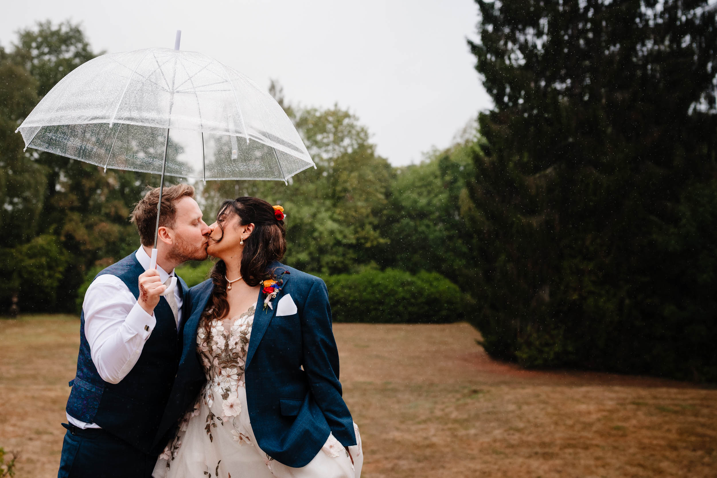 Anika and Sam sharing a kiss under a clear umbrella in the rain
