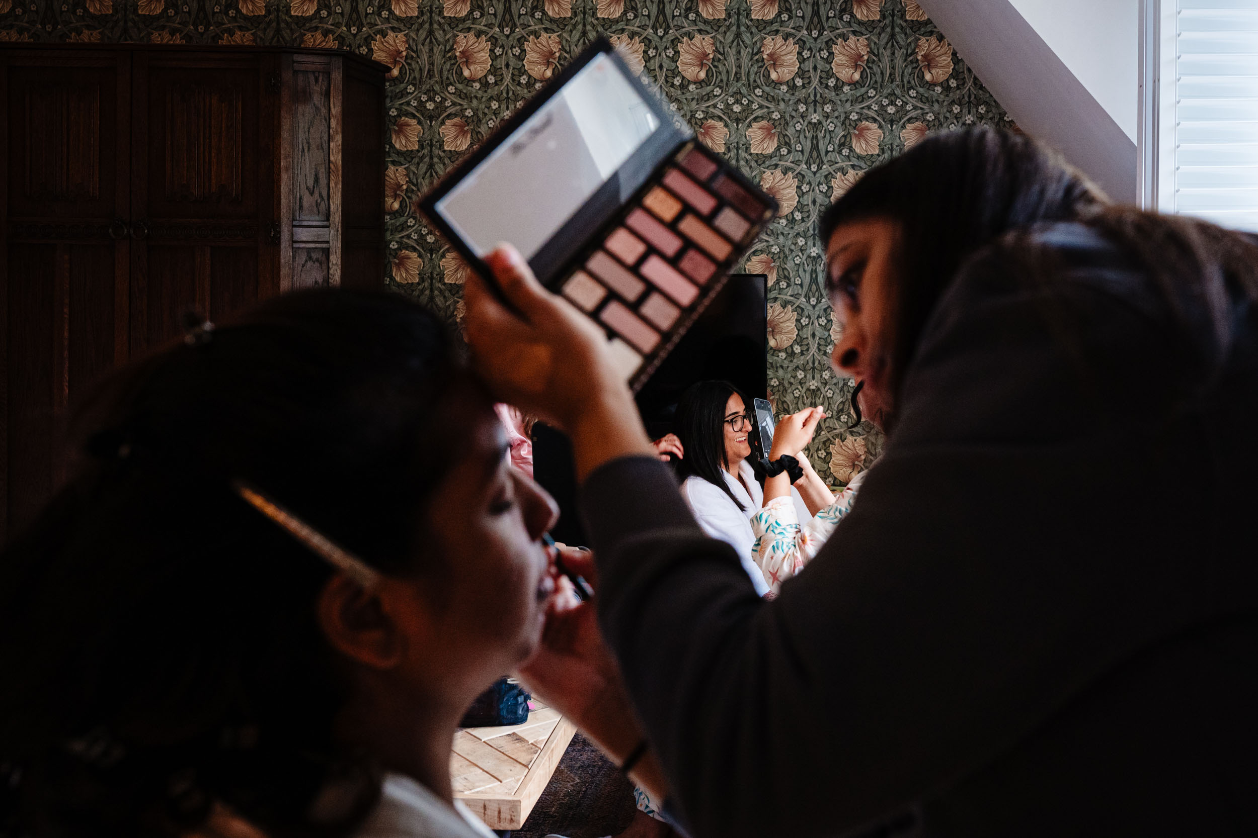 Photo taken through makeup artist and Anika showing bridesmaids laughing in the background
