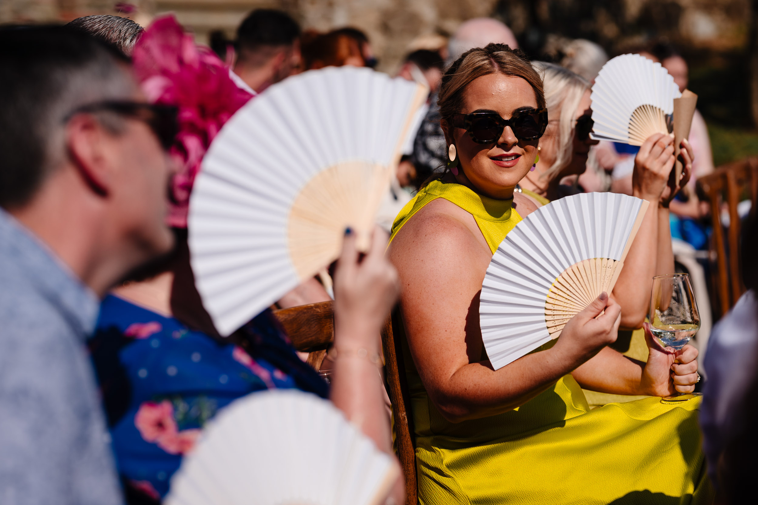 Guests using white fans to keep cool during the outdoor ceremony.