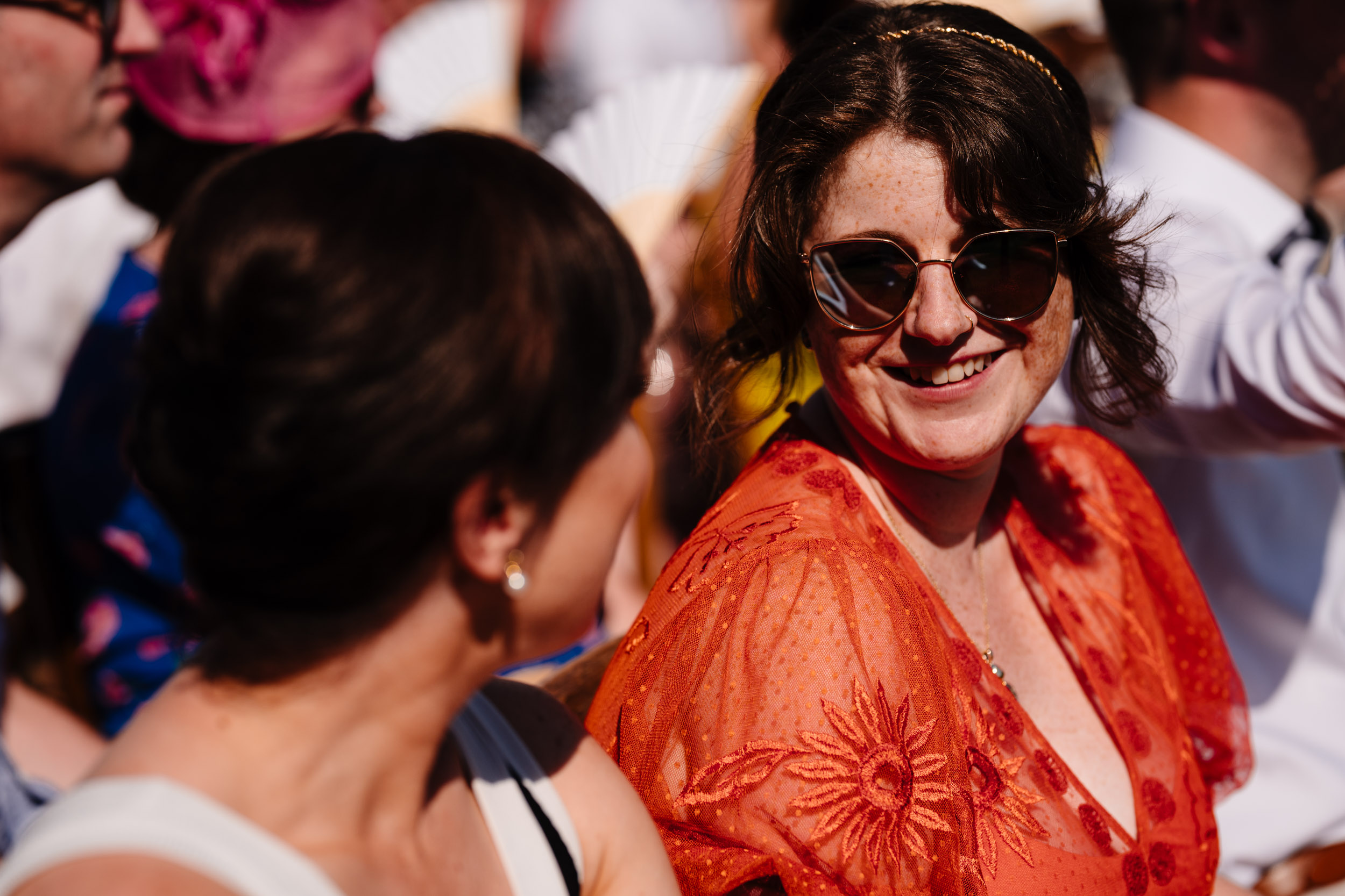 Wedding guest in sunglasses smiling during the ceremony.