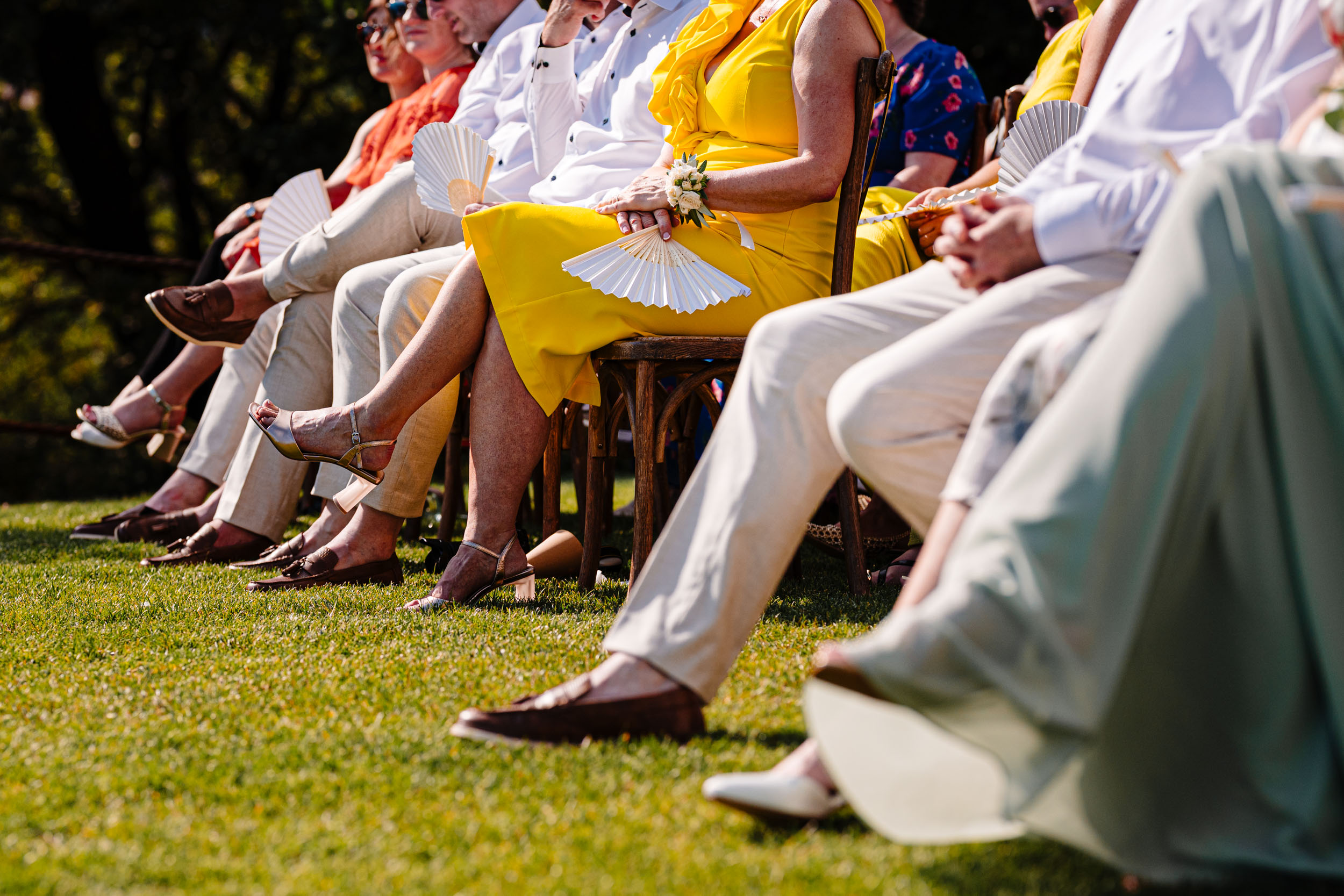Guests seated on the lawn with white fans during the warm ceremony.