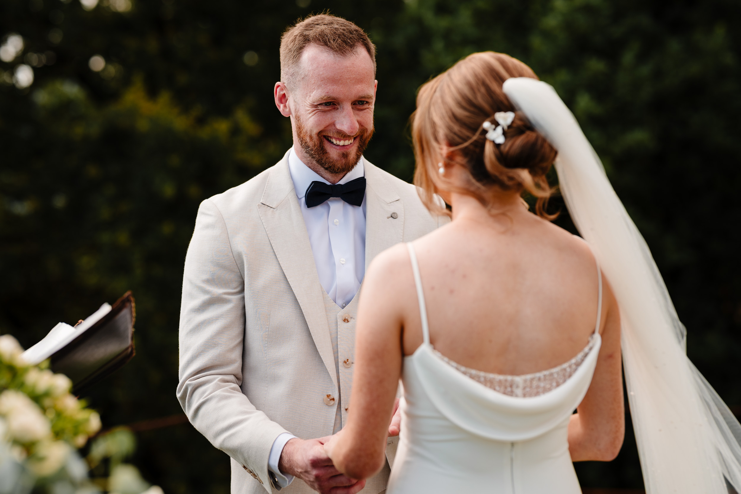 Groom smiling while holding the bride’s hands during their vows.