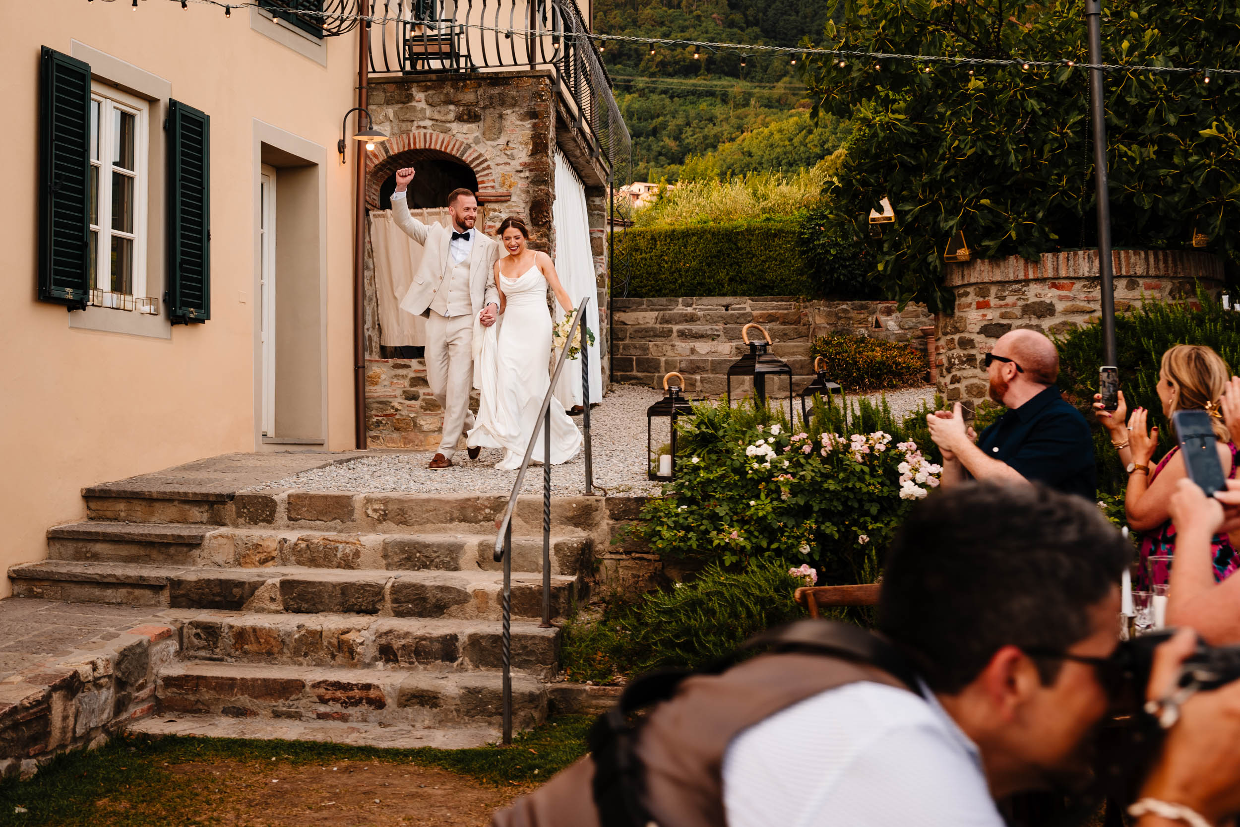Bride and groom walking down the stone steps into the dinner reception as guests applaud.