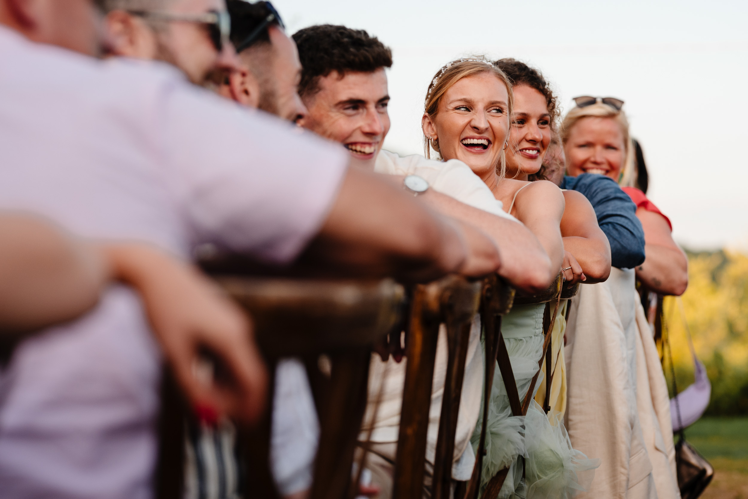 Group of guests leaning on the backs of chairs, laughing during the speeches.