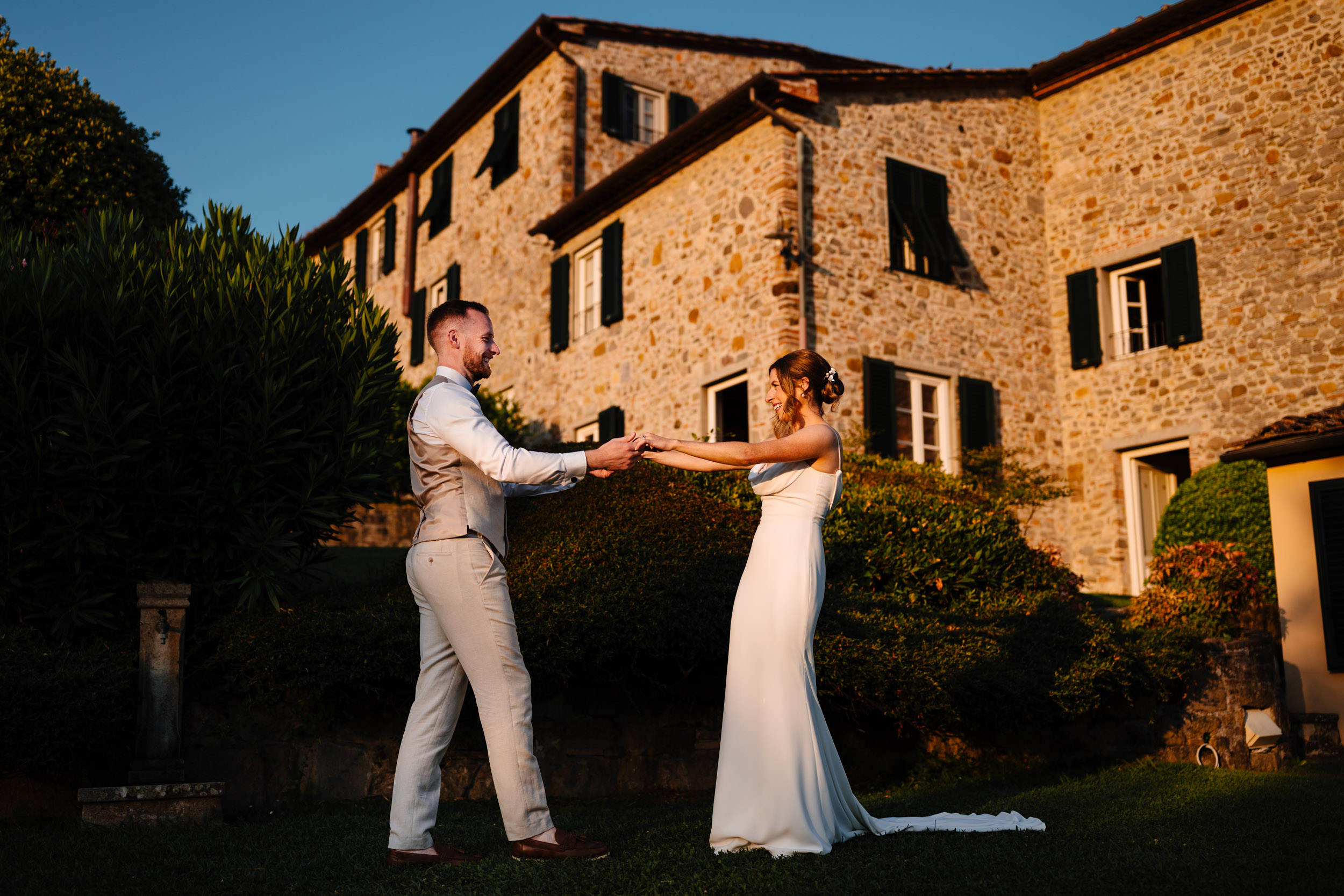 Bride and groom holding hands and dancing outside the villa at sunset.