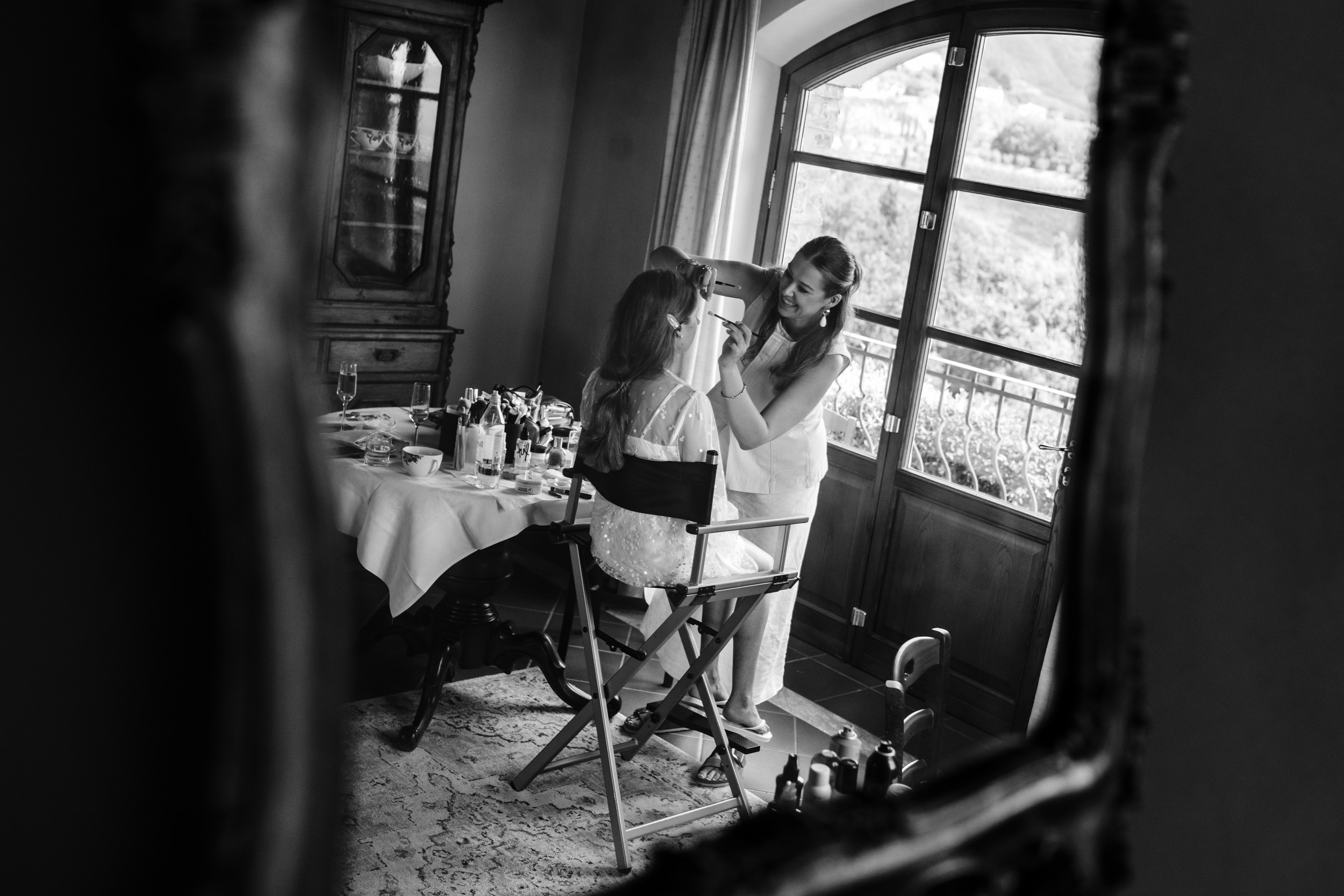 Bride having her makeup done in the Tuscan villa, reflected in a mirror.