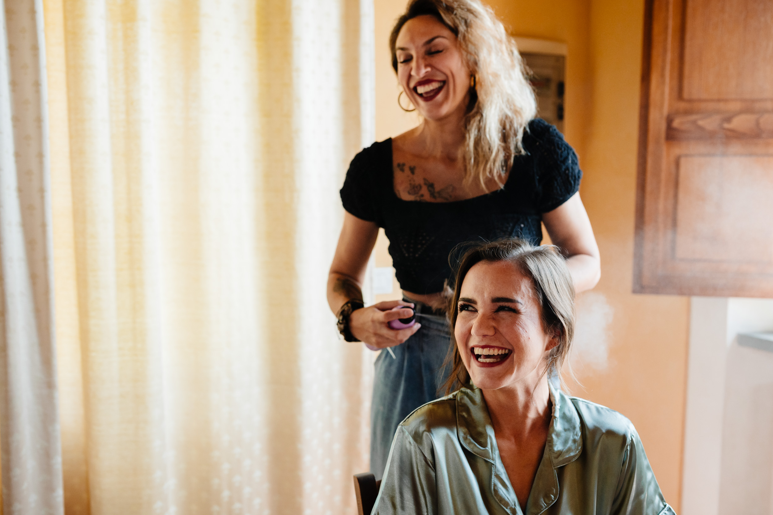 Bridesmaid laughing while getting her hair styled during the wedding morning.