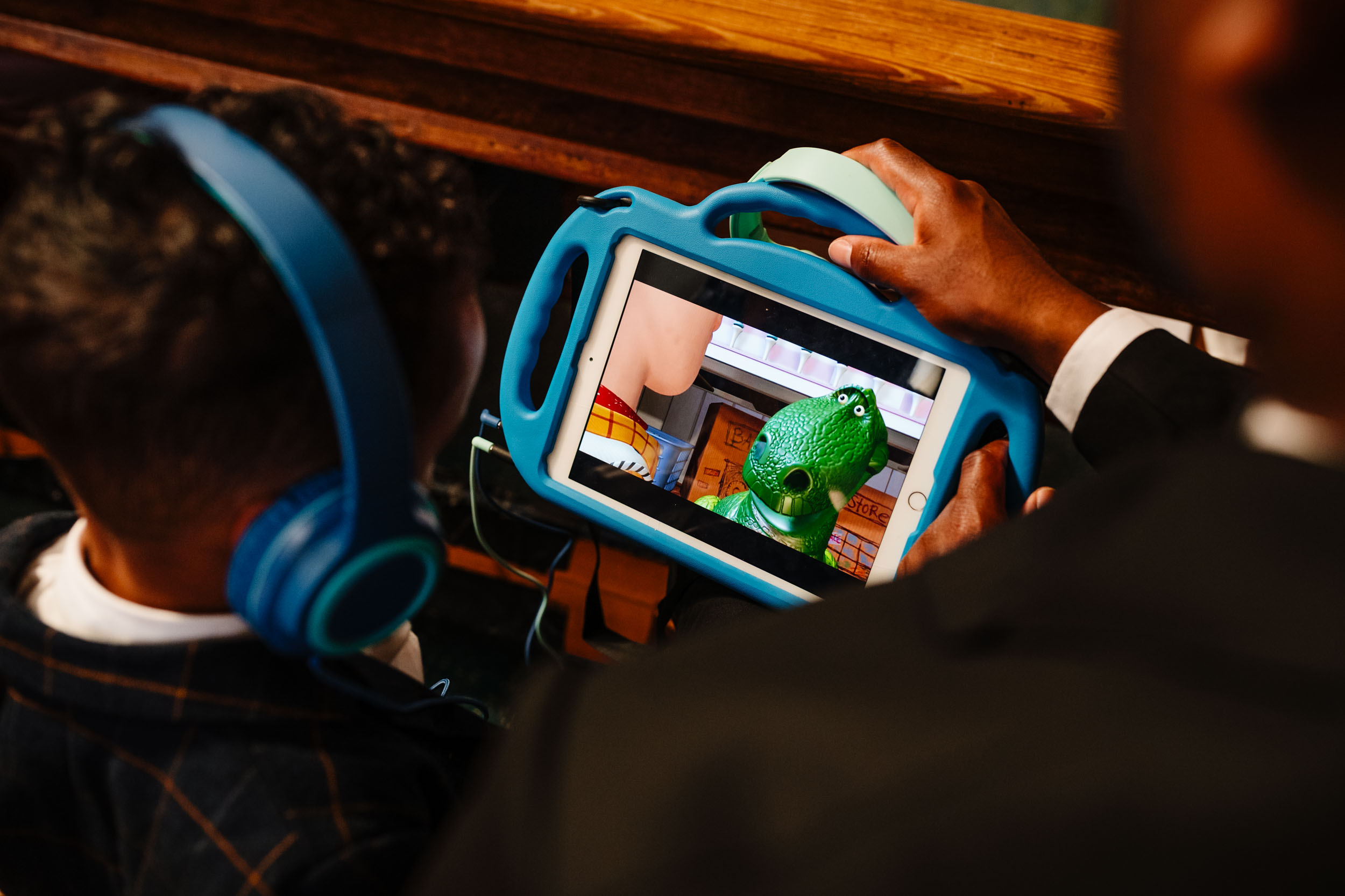 Child watching a cartoon on a tablet during the church ceremony, candid moment.