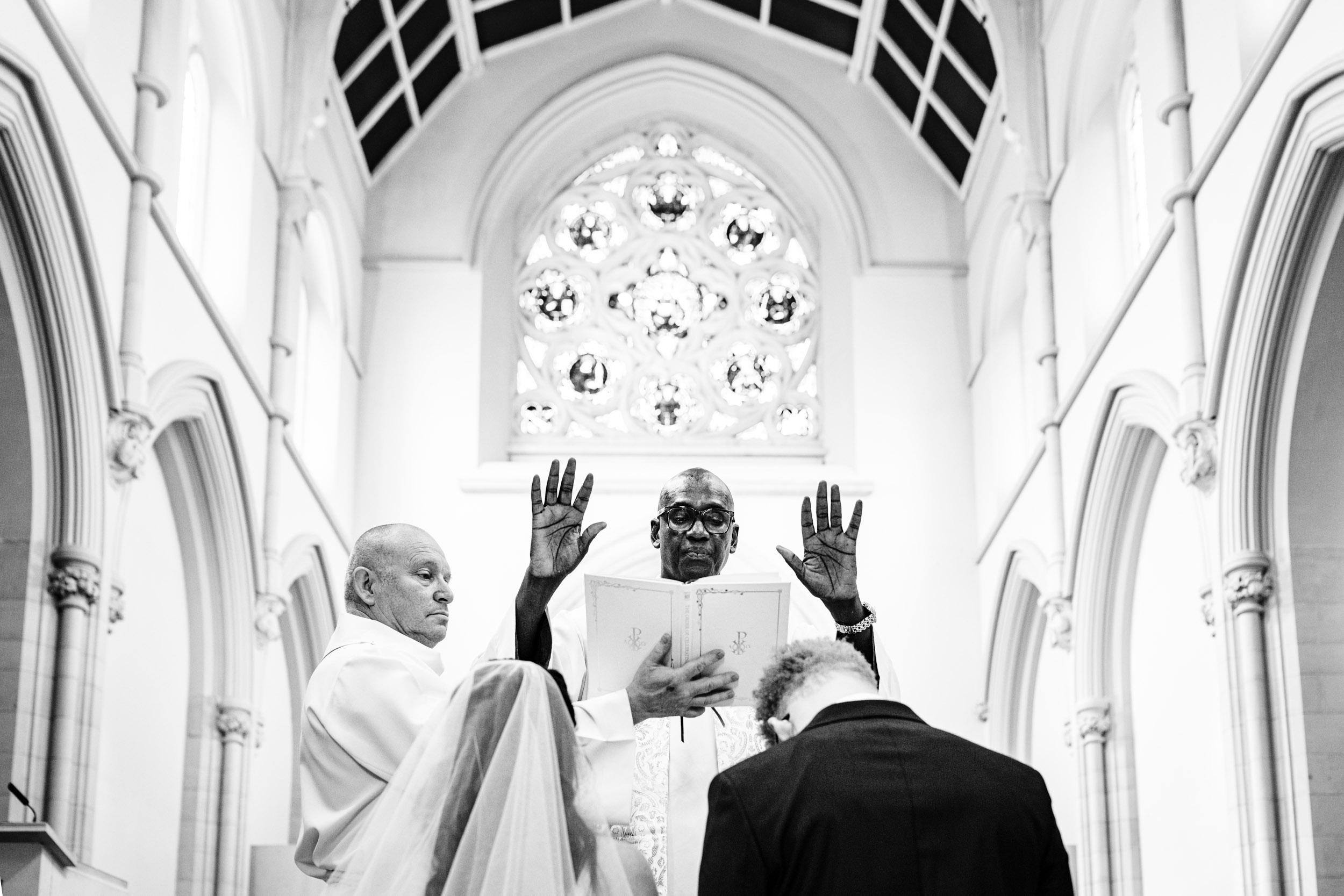 Priest raising his hands during the ceremony while Sylvia and Joe bow their heads.