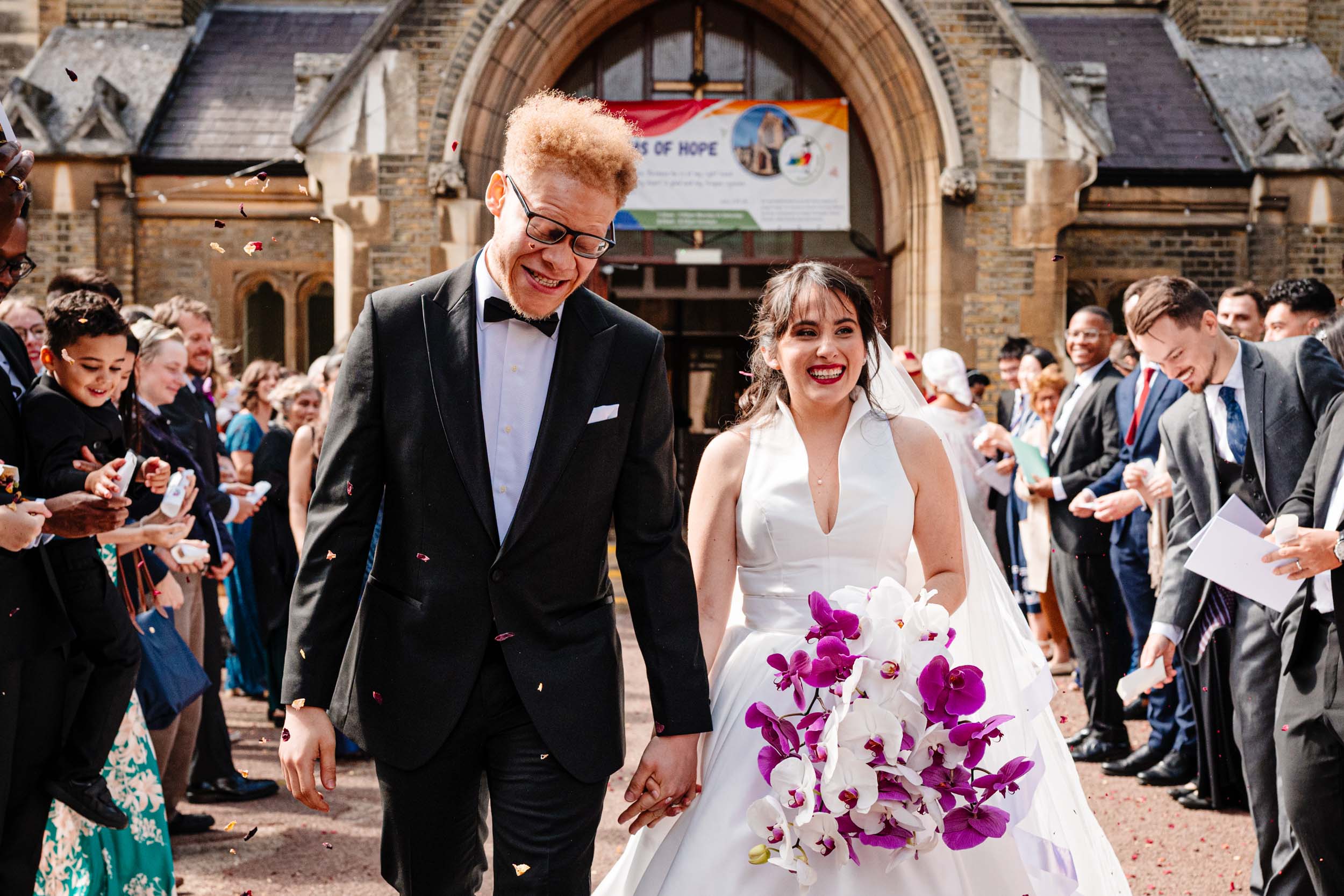 Bride and groom walking through a confetti throw outside the church, full of movement and smiles.