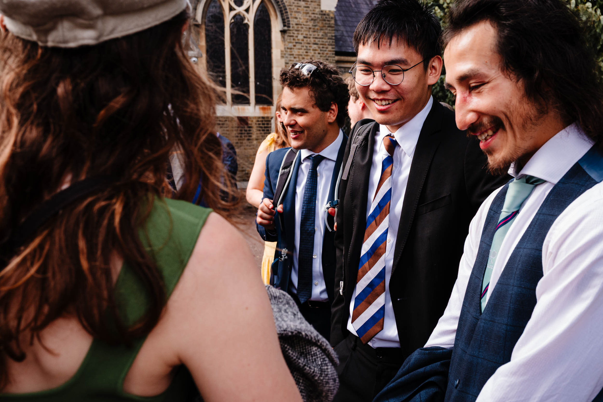 Wedding guests laughing and chatting in the church courtyard in Bow.