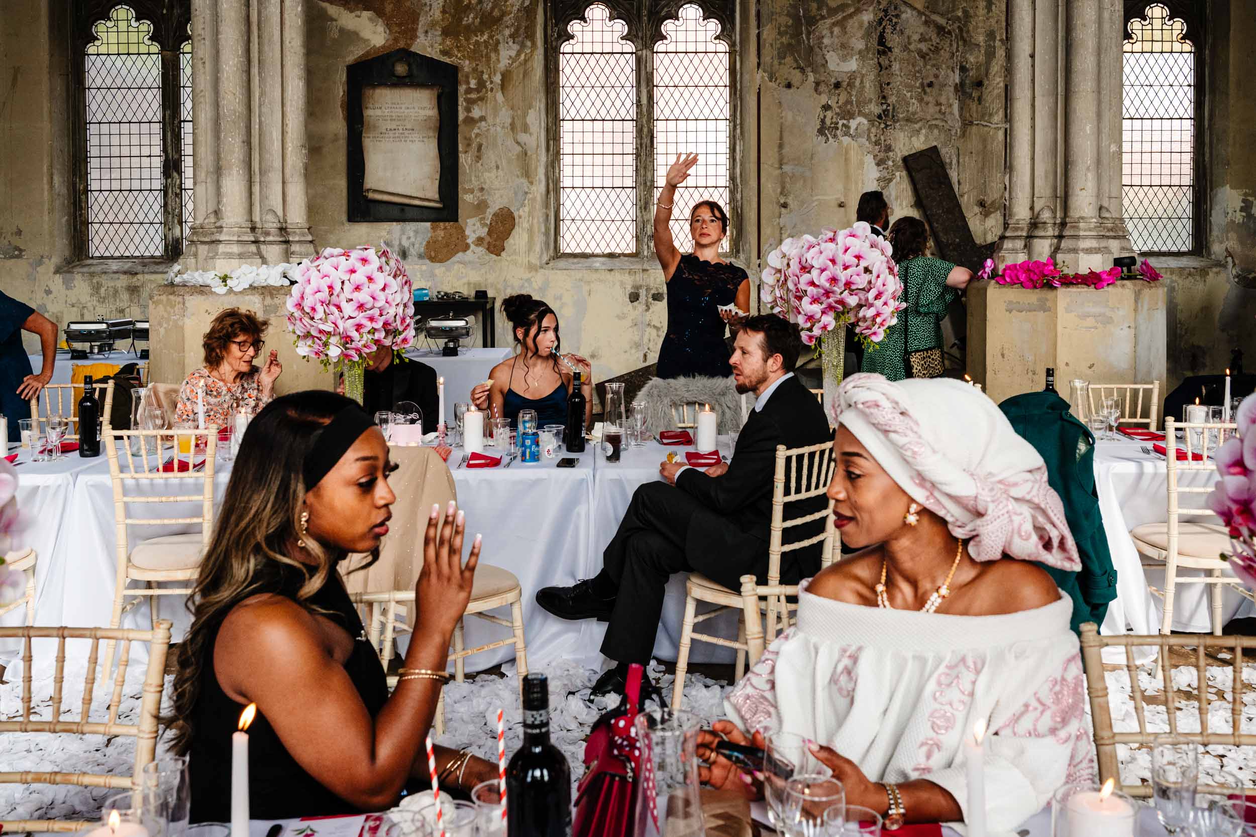 Layered scene at the long tables during the reception, guests talking and interacting in the foreground and background.