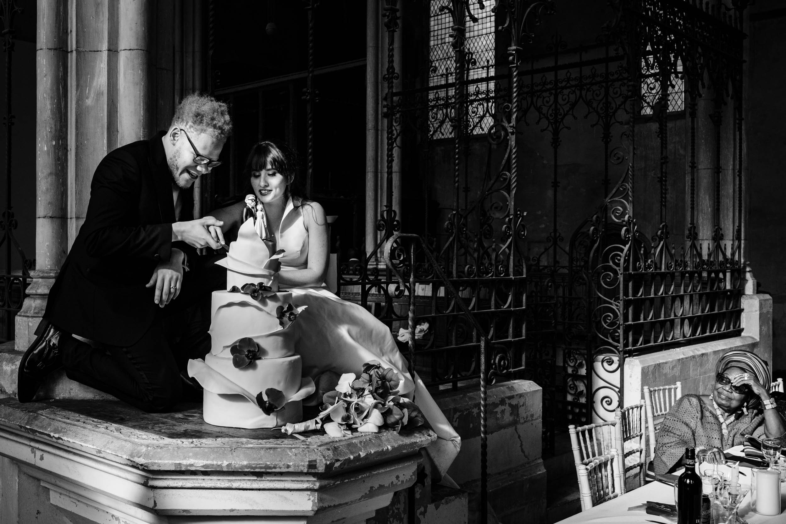 Bride and groom cutting their wedding cake, with Joe’s nan reacting joyfully in the corner of the frame.