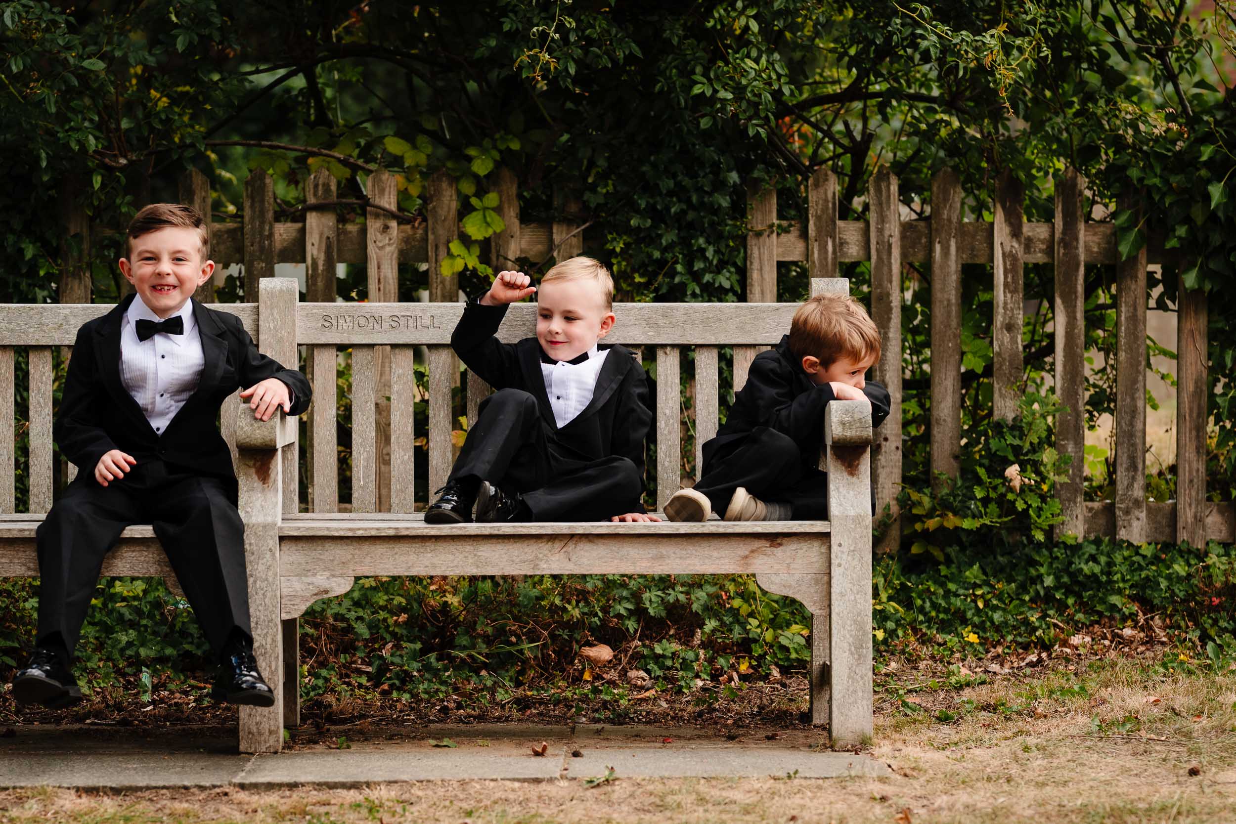 Three cheeky boys on a bench, one grinning at the camera, one looking away, one pulling a funny expression