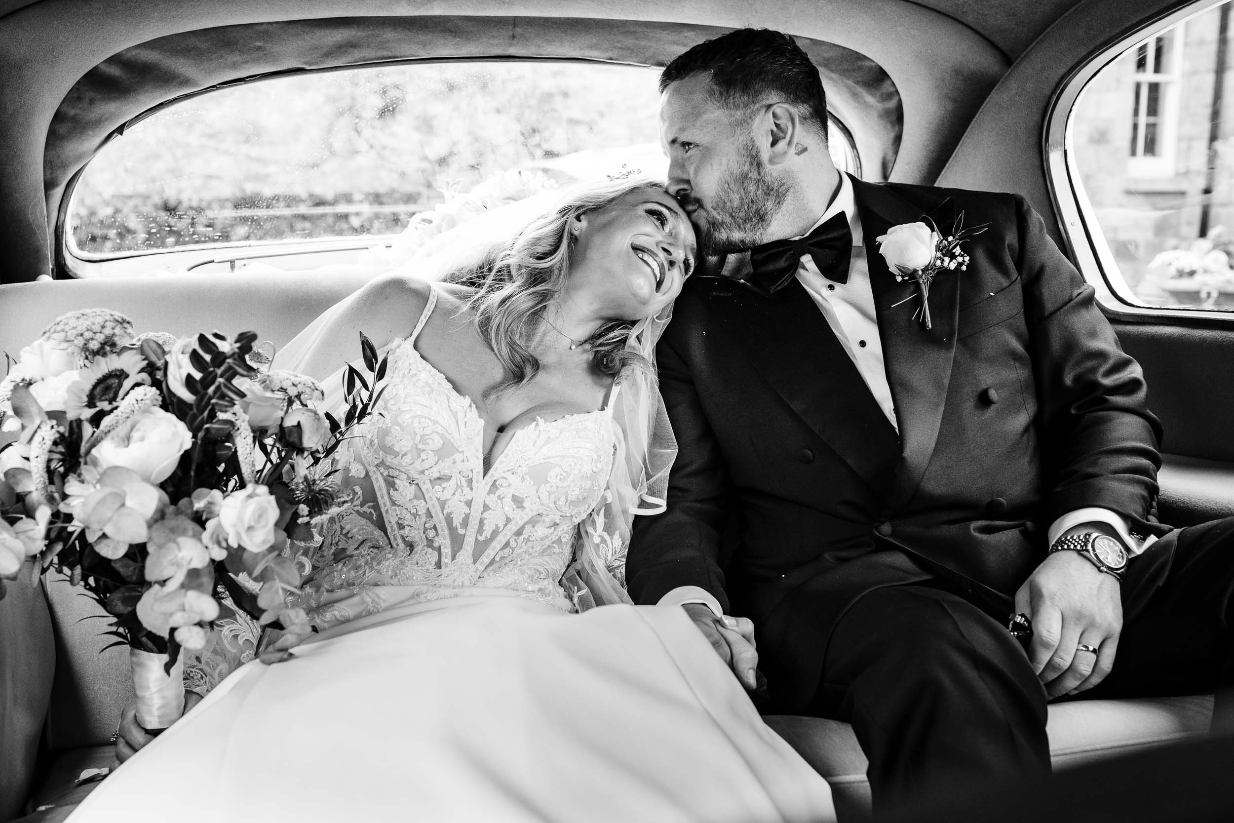 Bride and groom kissing inside the wedding car