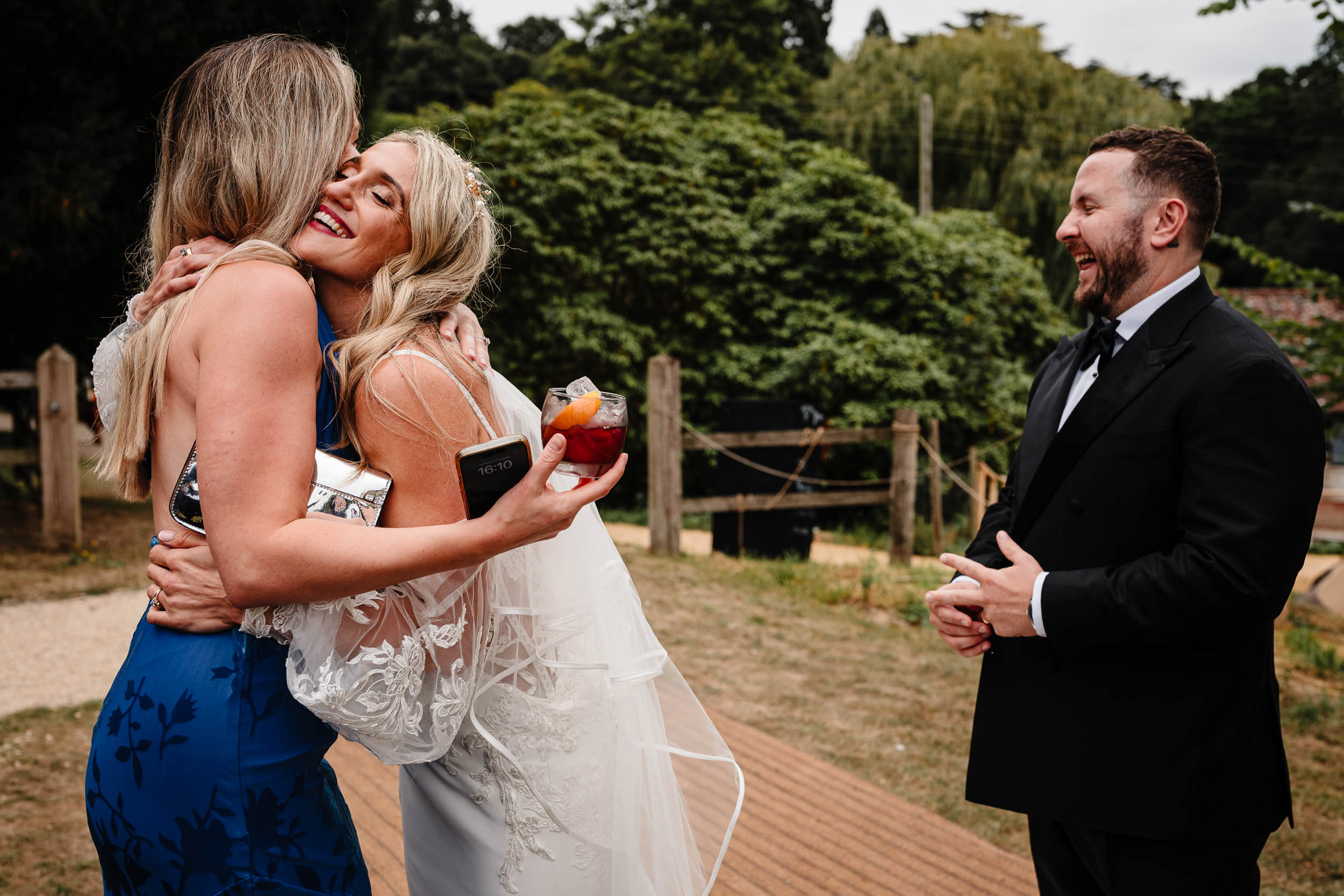 Bride hugging a guest while the groom laughs in the background