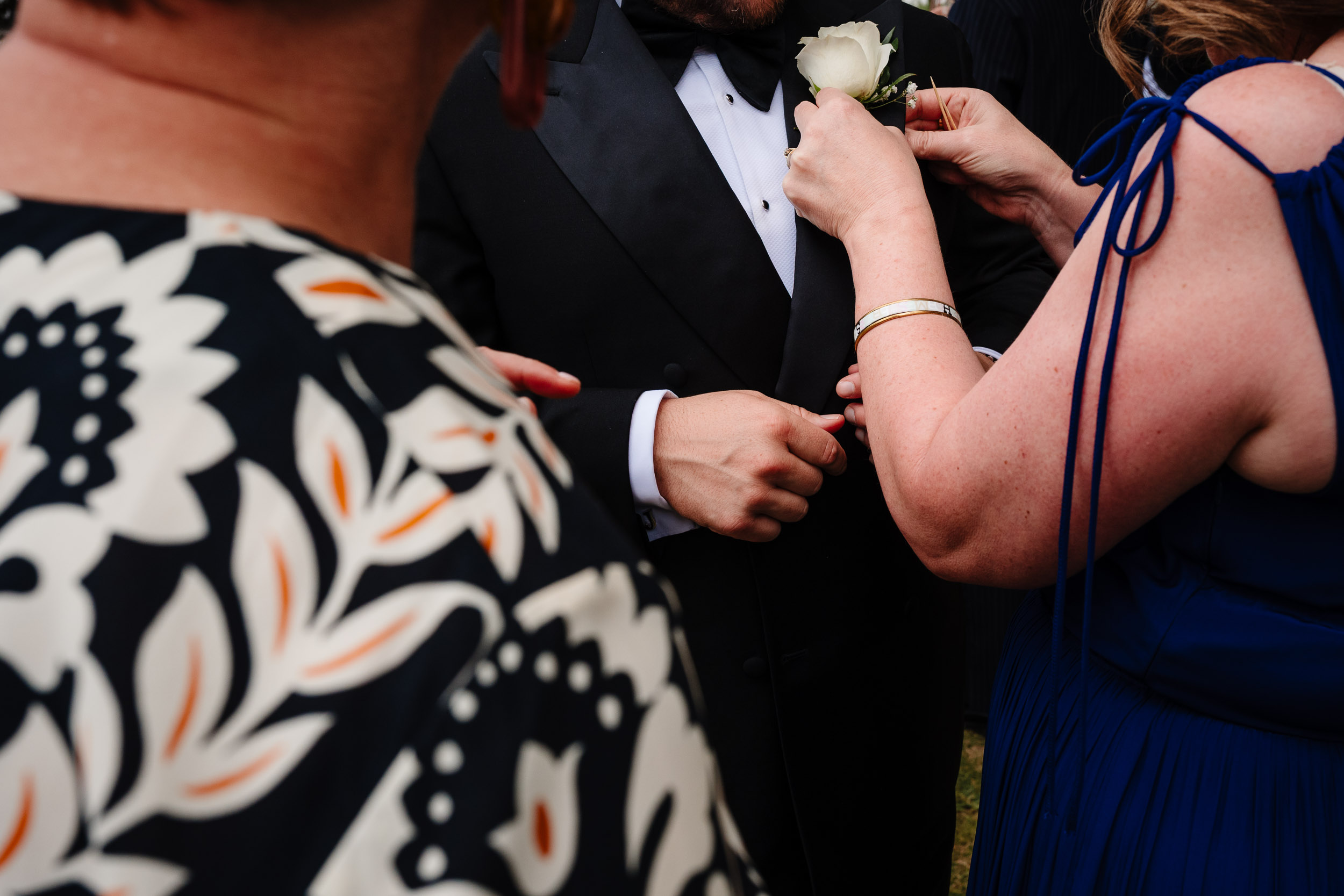 Guests fixing the groom’s buttonhole flower outside the pub