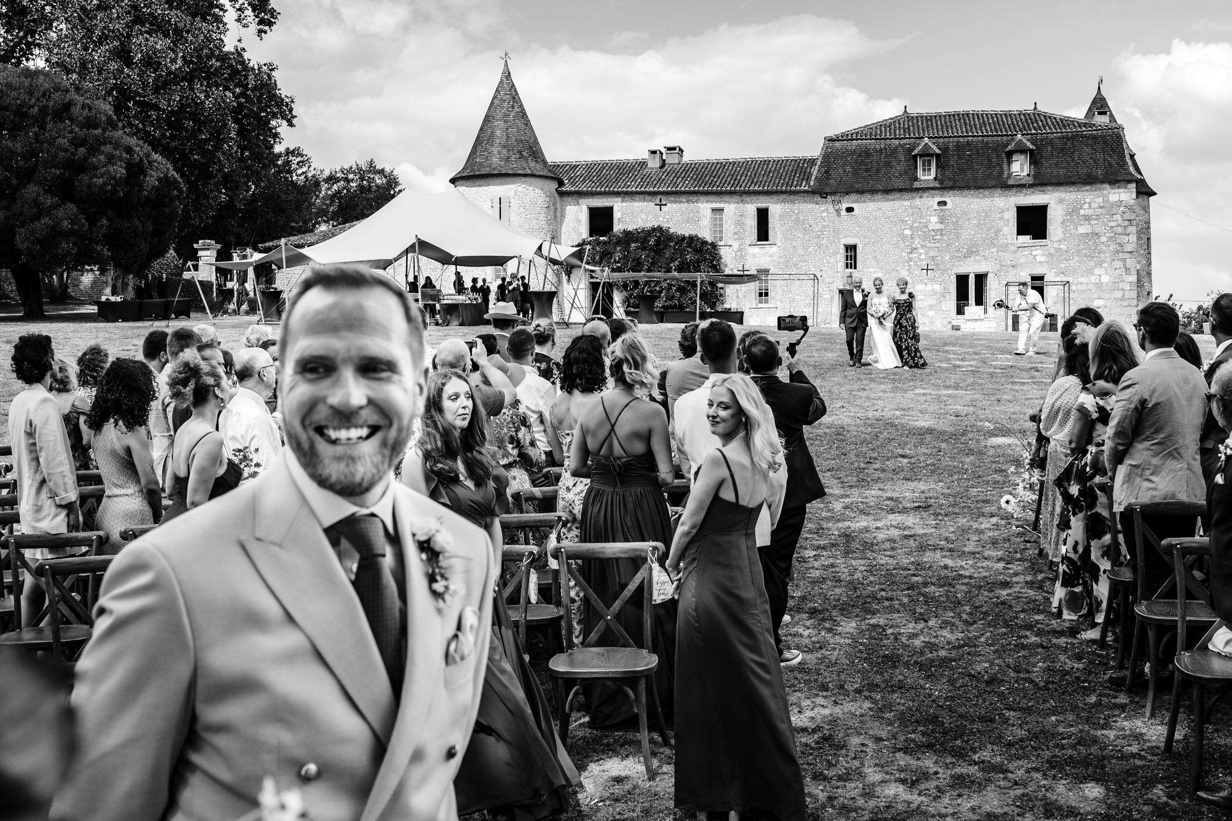 Groom smiling in the foreground as the bride walks towards the aisle in the background