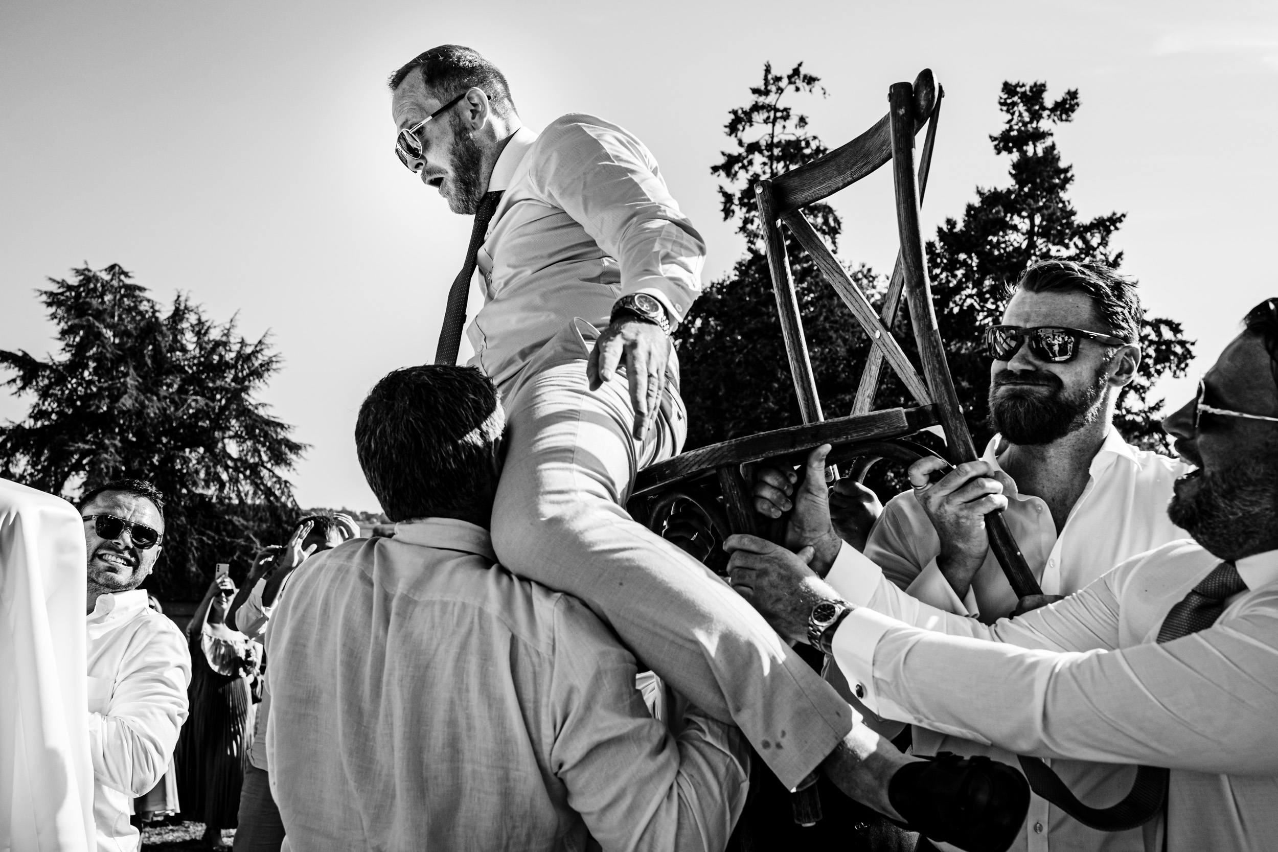 Groom being lifted into the air on a chair by wedding guests during Israeli dancing