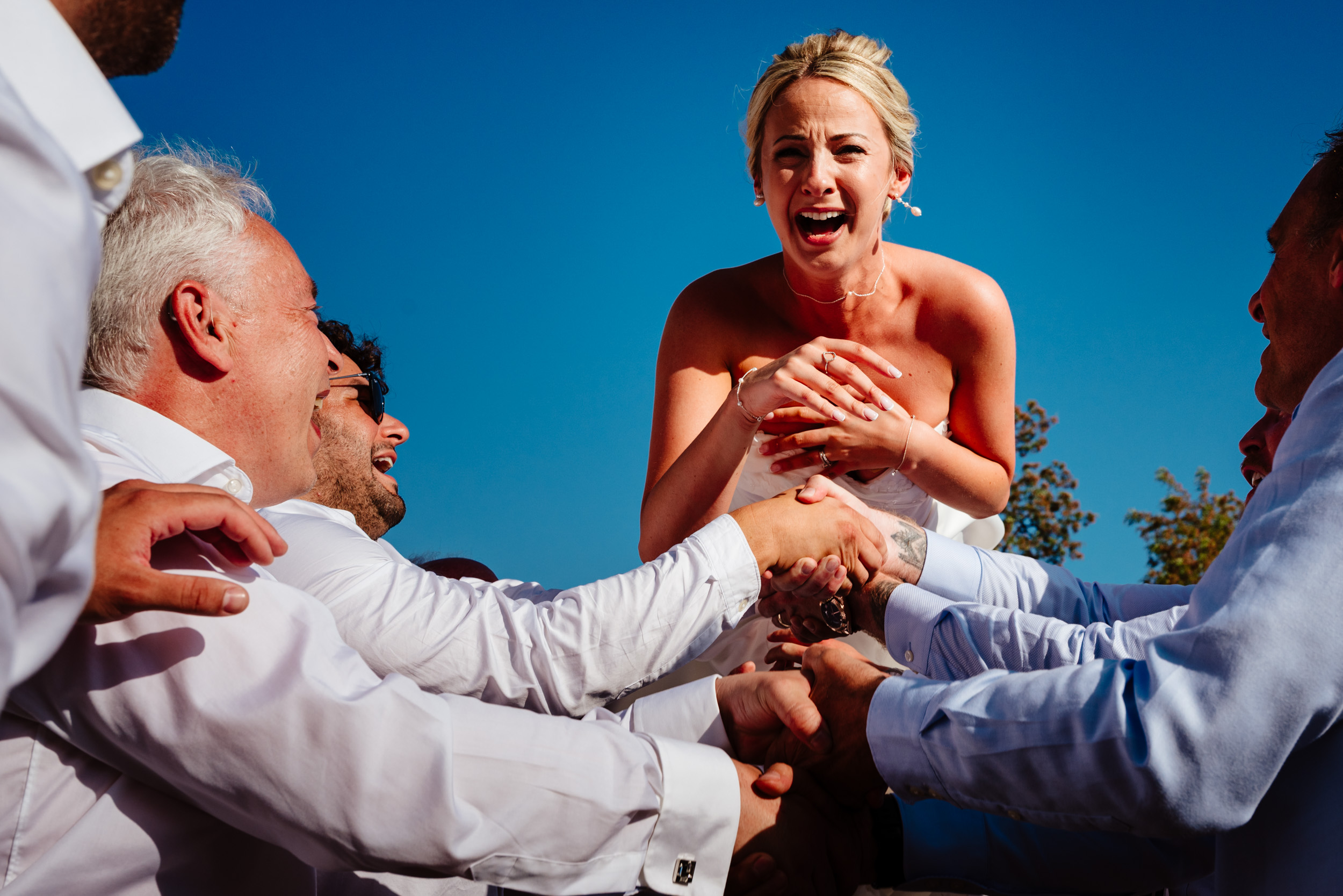 Bride mid-air during Israeli dancing with sunlight on her face and an excited expression