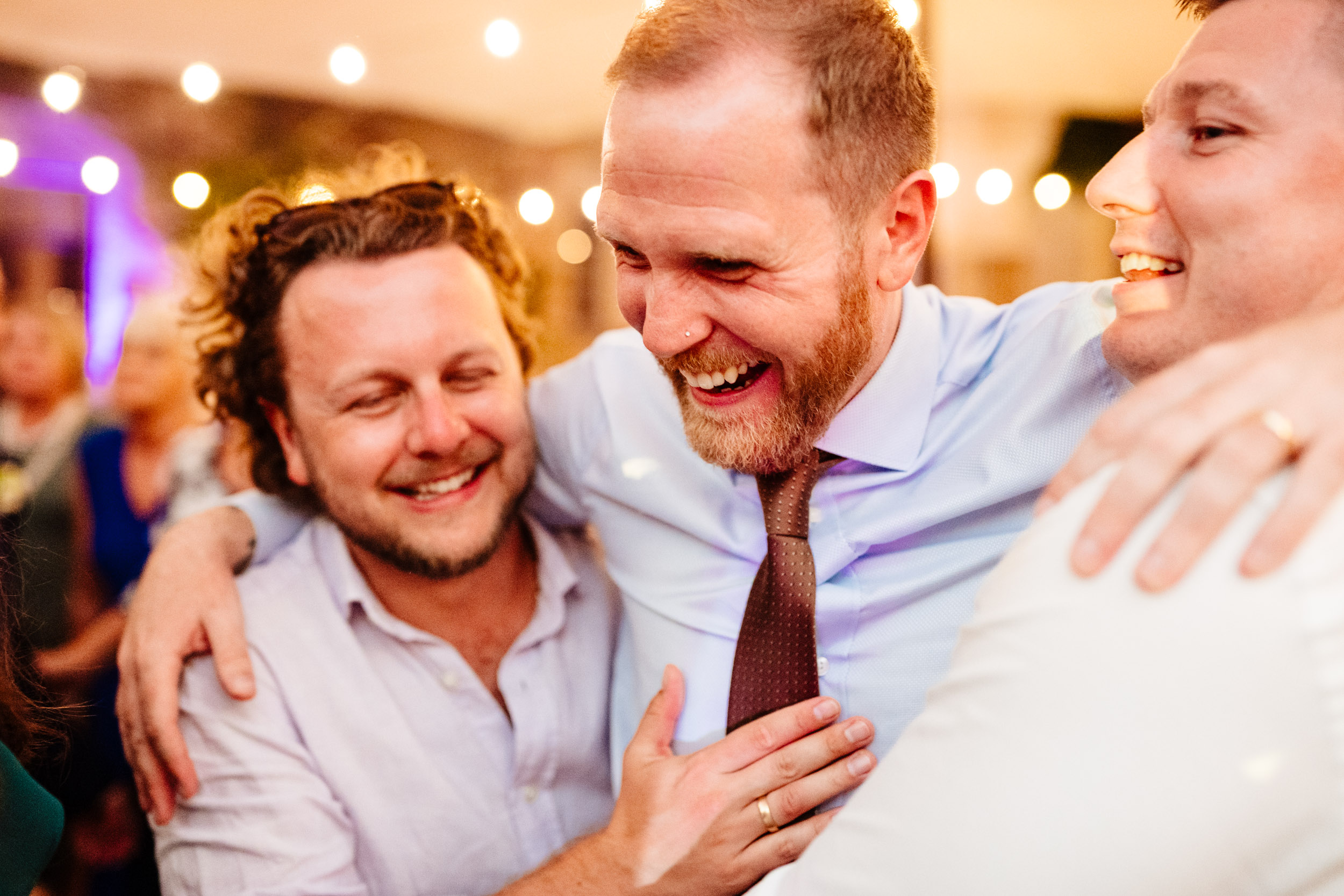 Groom hugging and laughing with friends on the dance floor