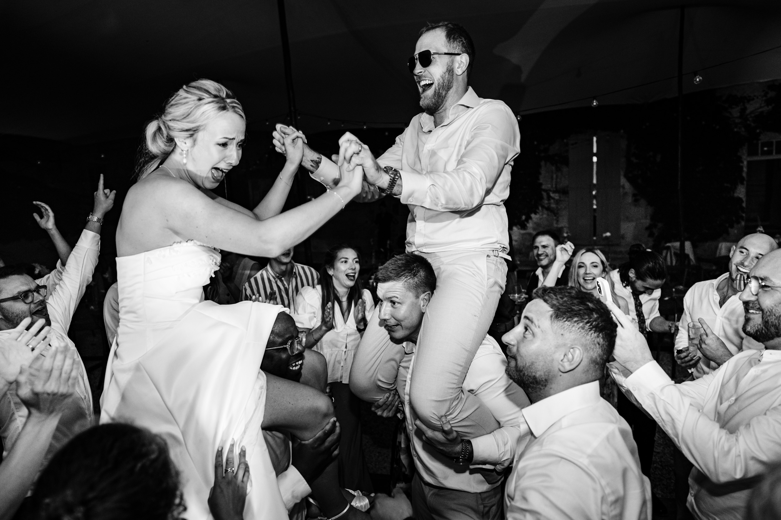 Bride and groom being lifted into the air on guests’ shoulders during the party