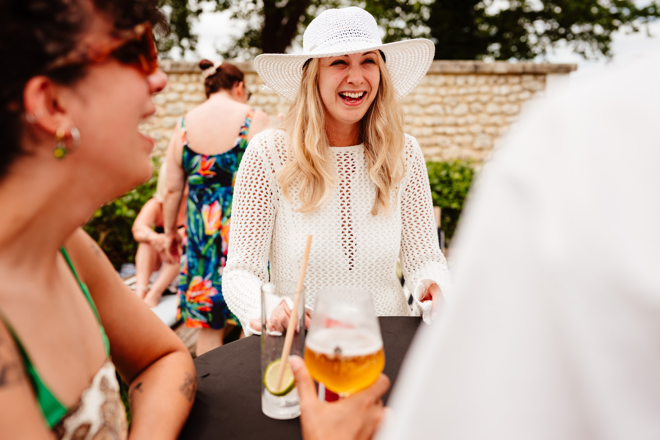 Bride laughing with guests around a table during the pool party