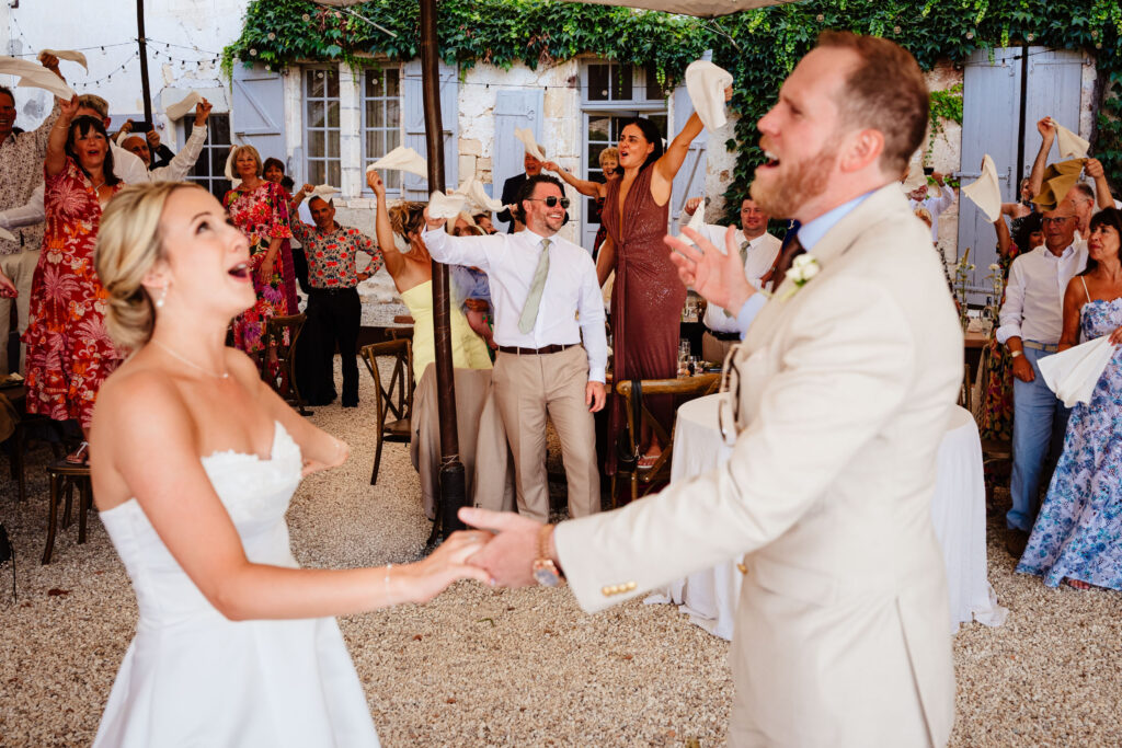 Bride and groom entering the dining area while guests wave napkins and celebrate