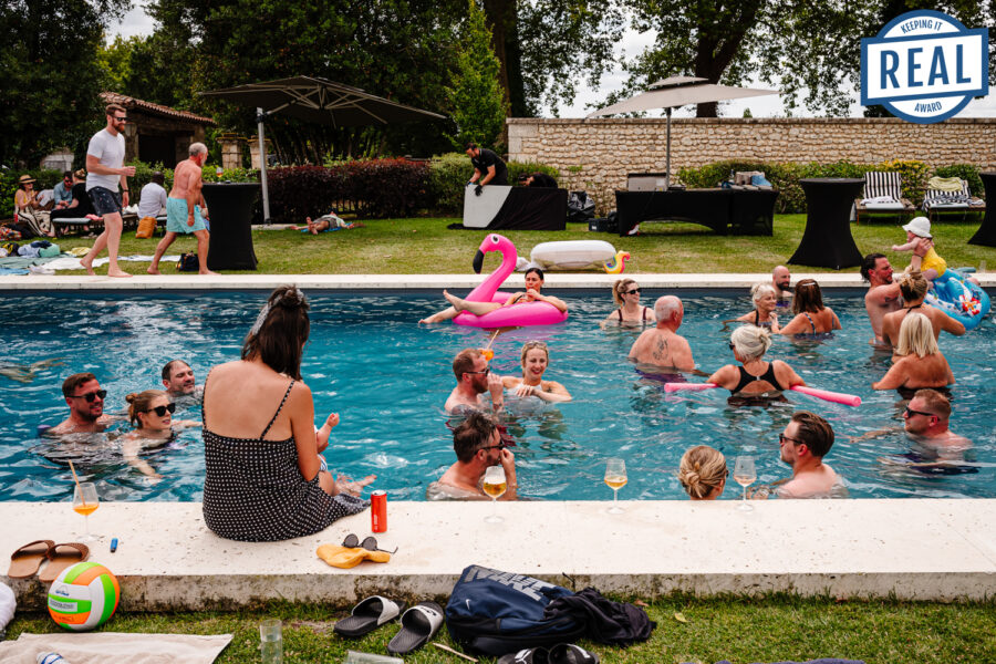 Busy pool party scene with guests in the water, featuring an award-winning wedding photograph badge