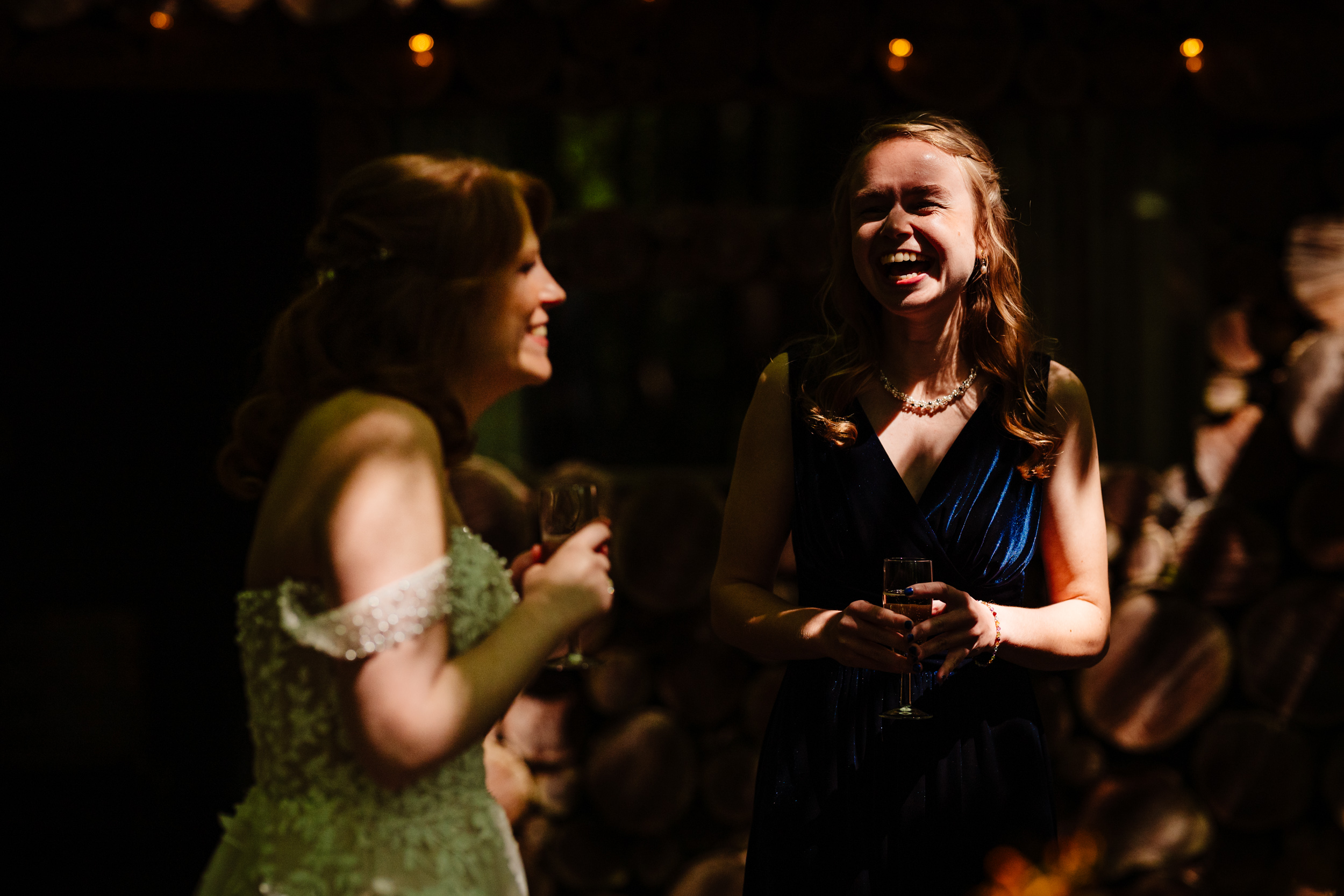 Bride and bridesmaid laughing together in dappled sunlight outside the venue