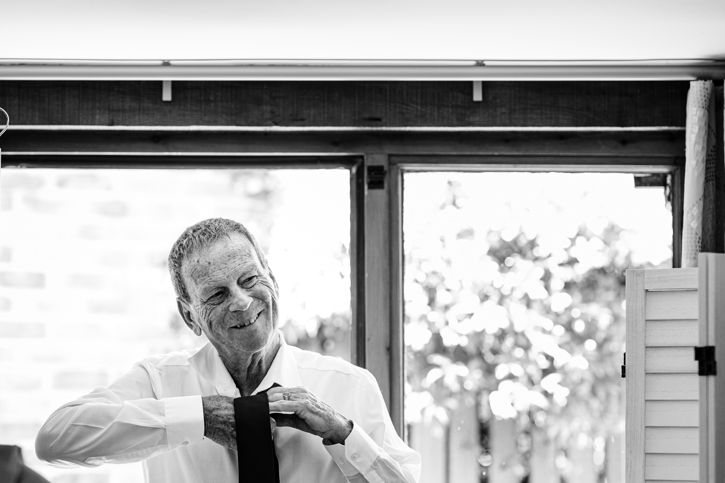 Bride’s dad concentrating as he adjusts his tie during morning preparations
