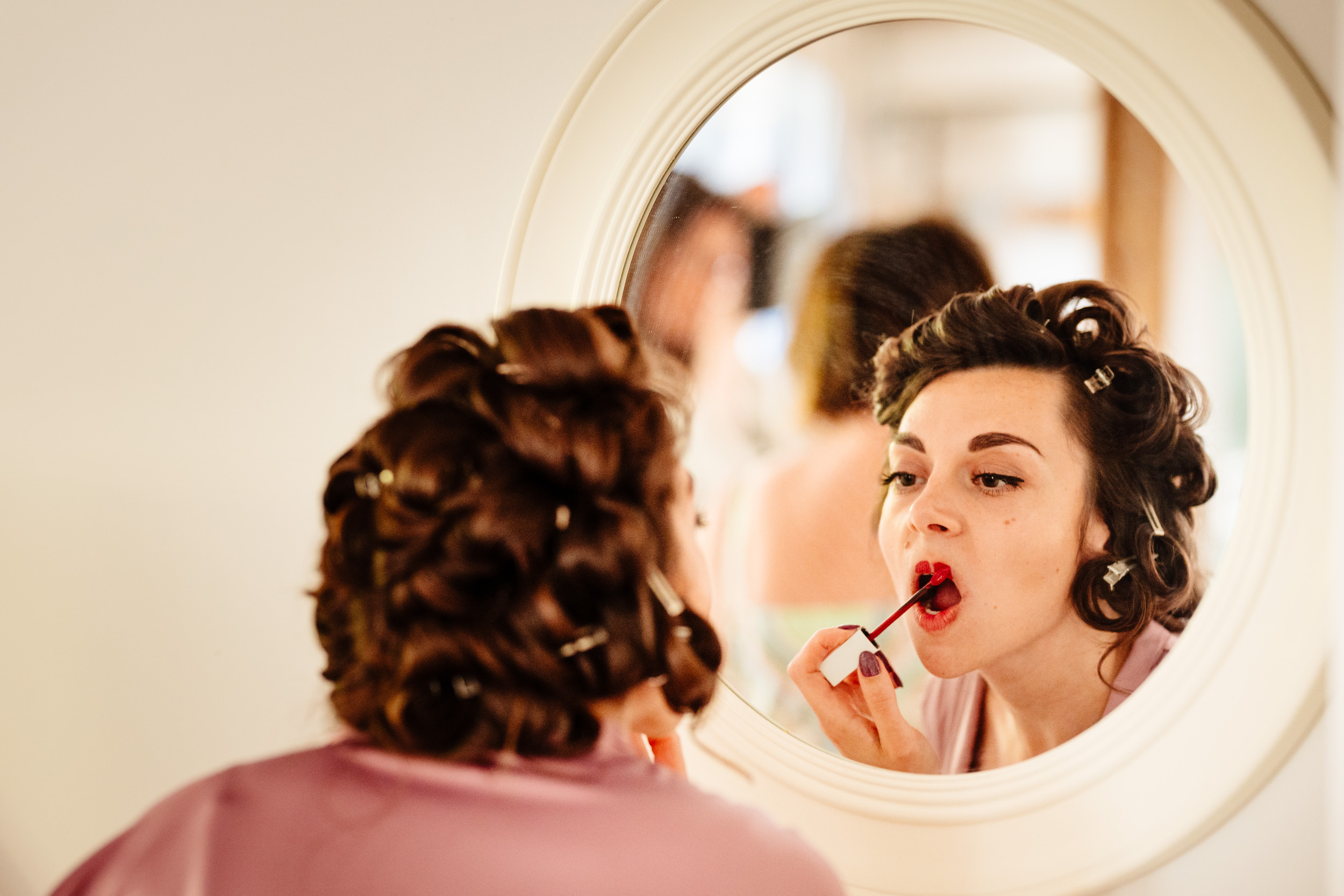 Bridesmaid applying lipstick while looking into the mirror during wedding preparations