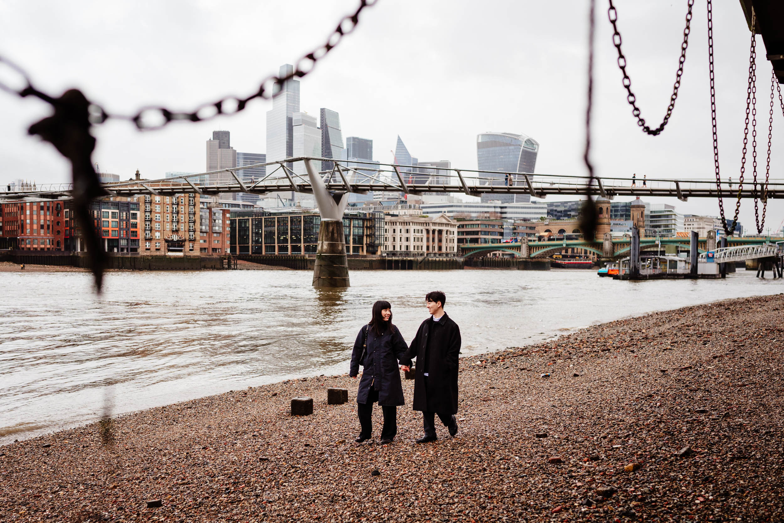 Couple walking along the riverside beach near St Paul’s Cathedral after getting engaged.