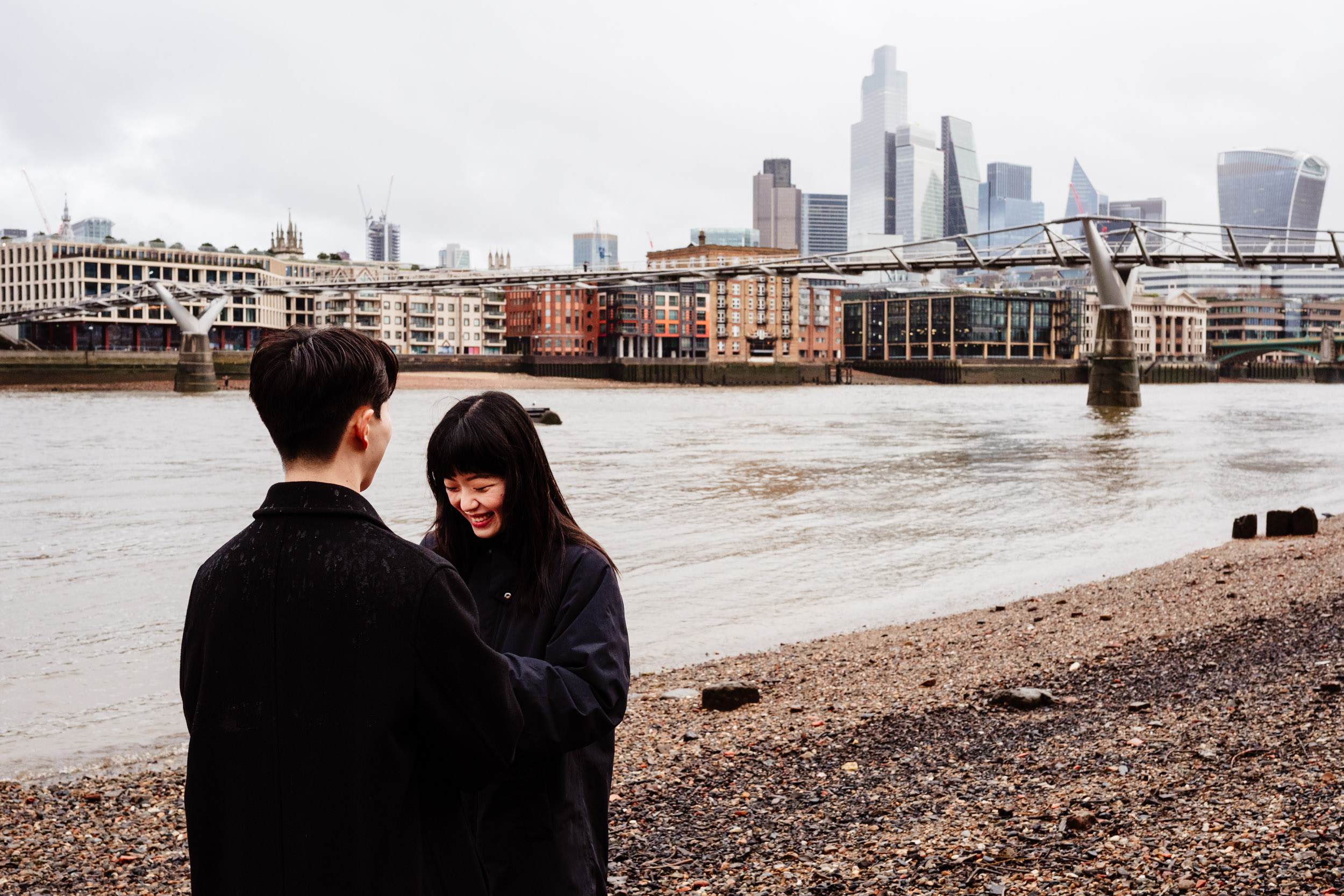 She laughs on the riverside beach following their surprise proposal in London.