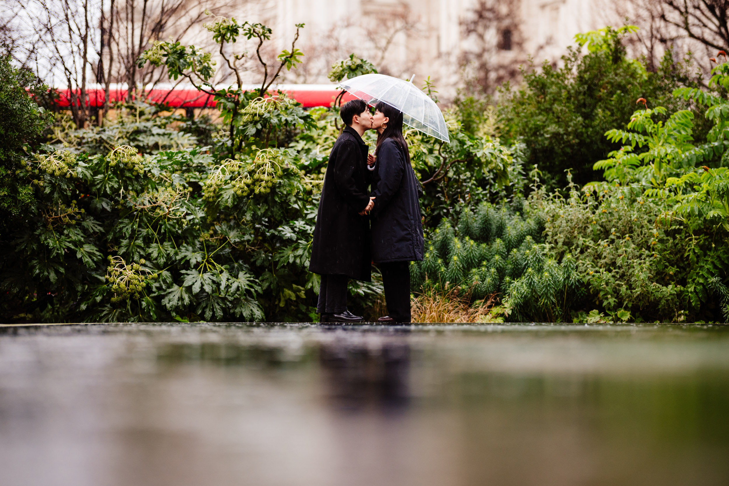 Couple sharing a kiss under a clear umbrella after their surprise proposal at St Paul’s Cathedral.