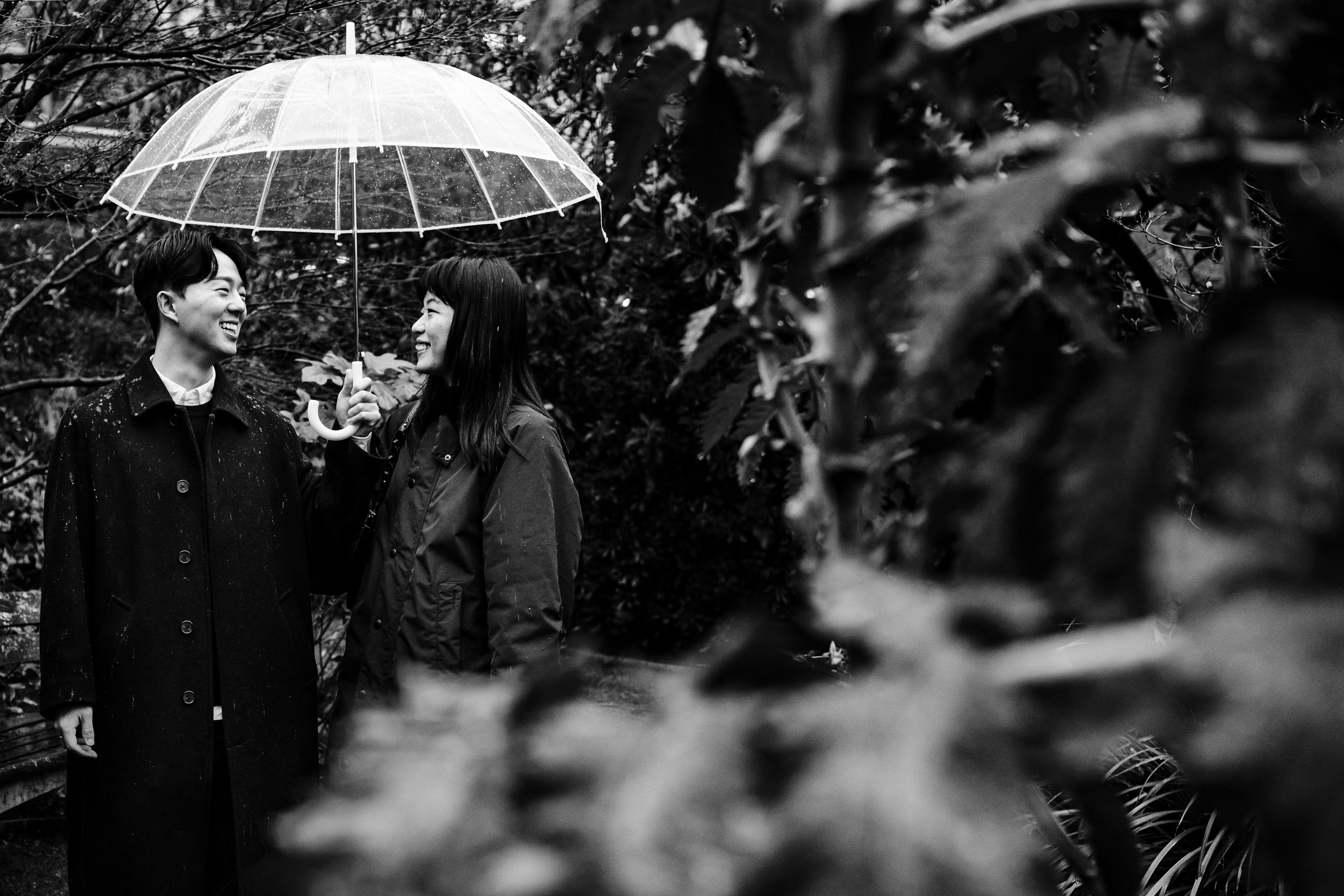 Newly engaged couple walking under an umbrella, laughing after their St Paul’s Cathedral proposal.