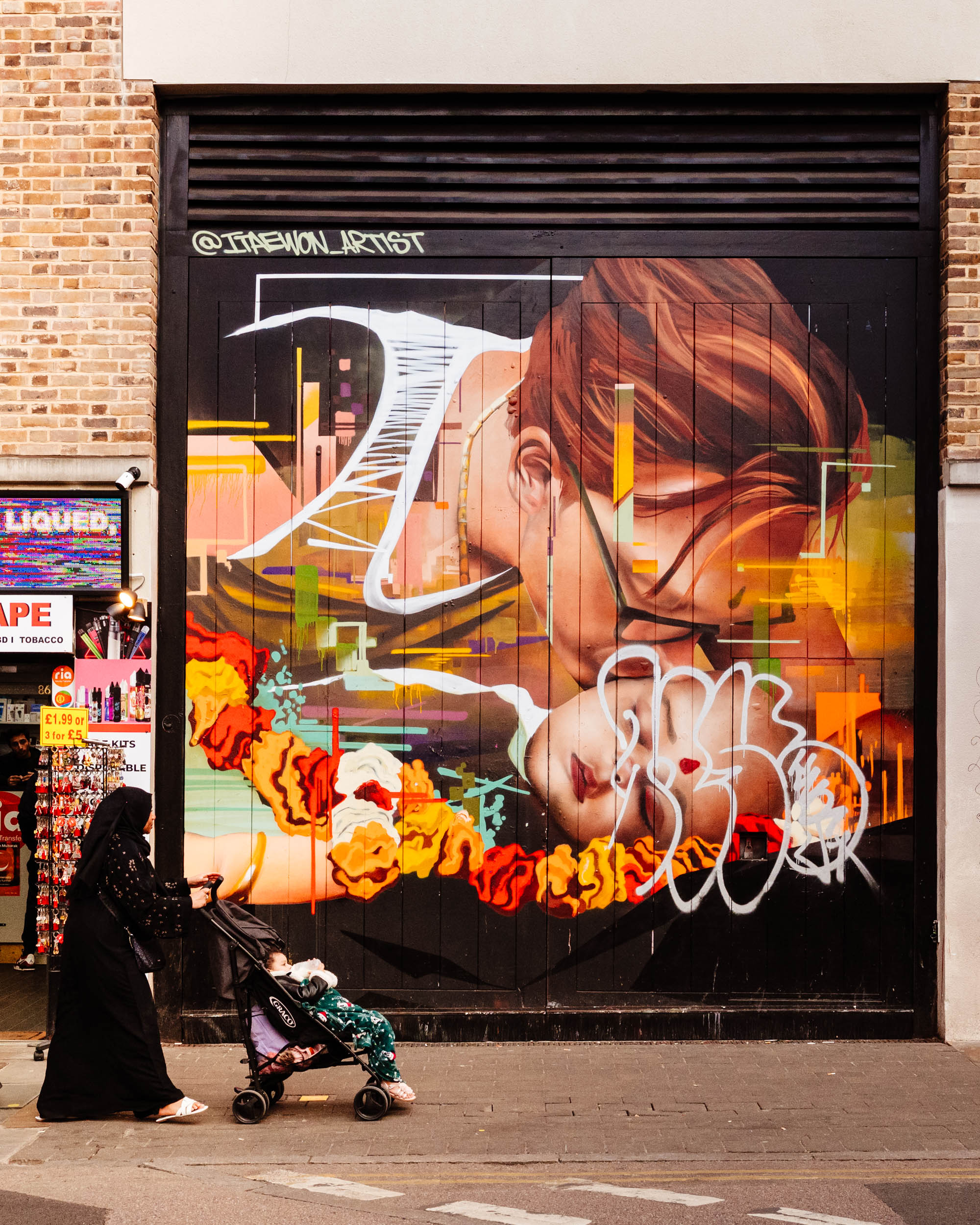 Mother pushes a stroller in front of a maternal poster near Brick Lane in London.