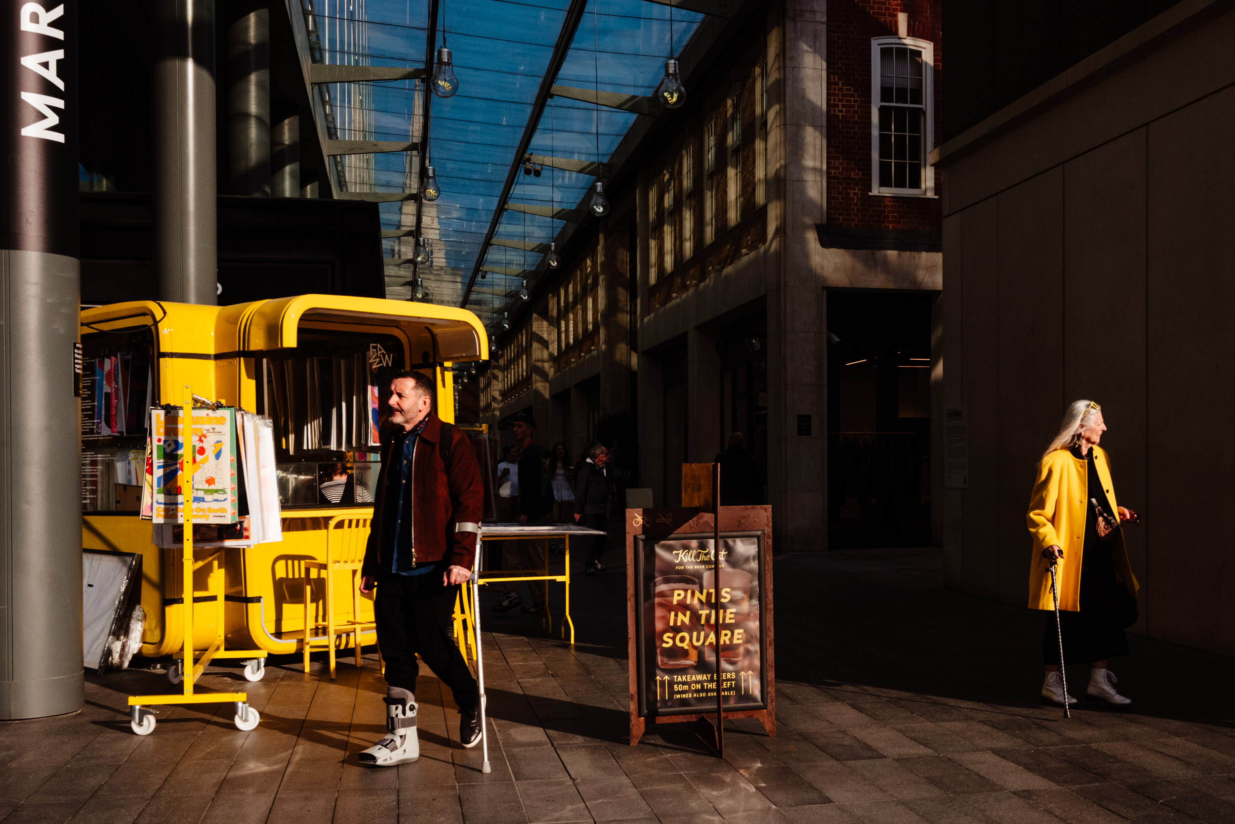 Two people walk in different directions, illuminated by the sun, both having walking sticks.