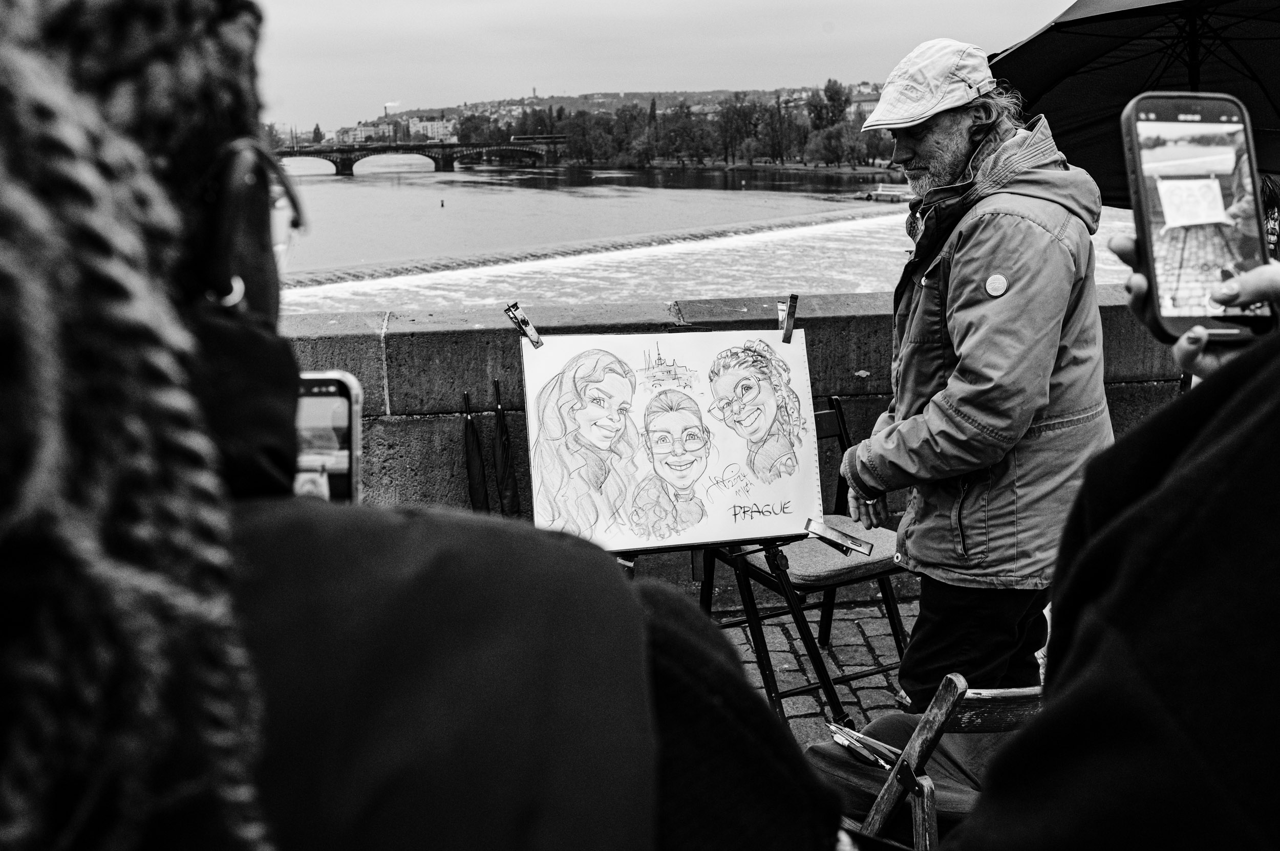 Artist drawing on Charles Bridge in Prague while people take photos of him.