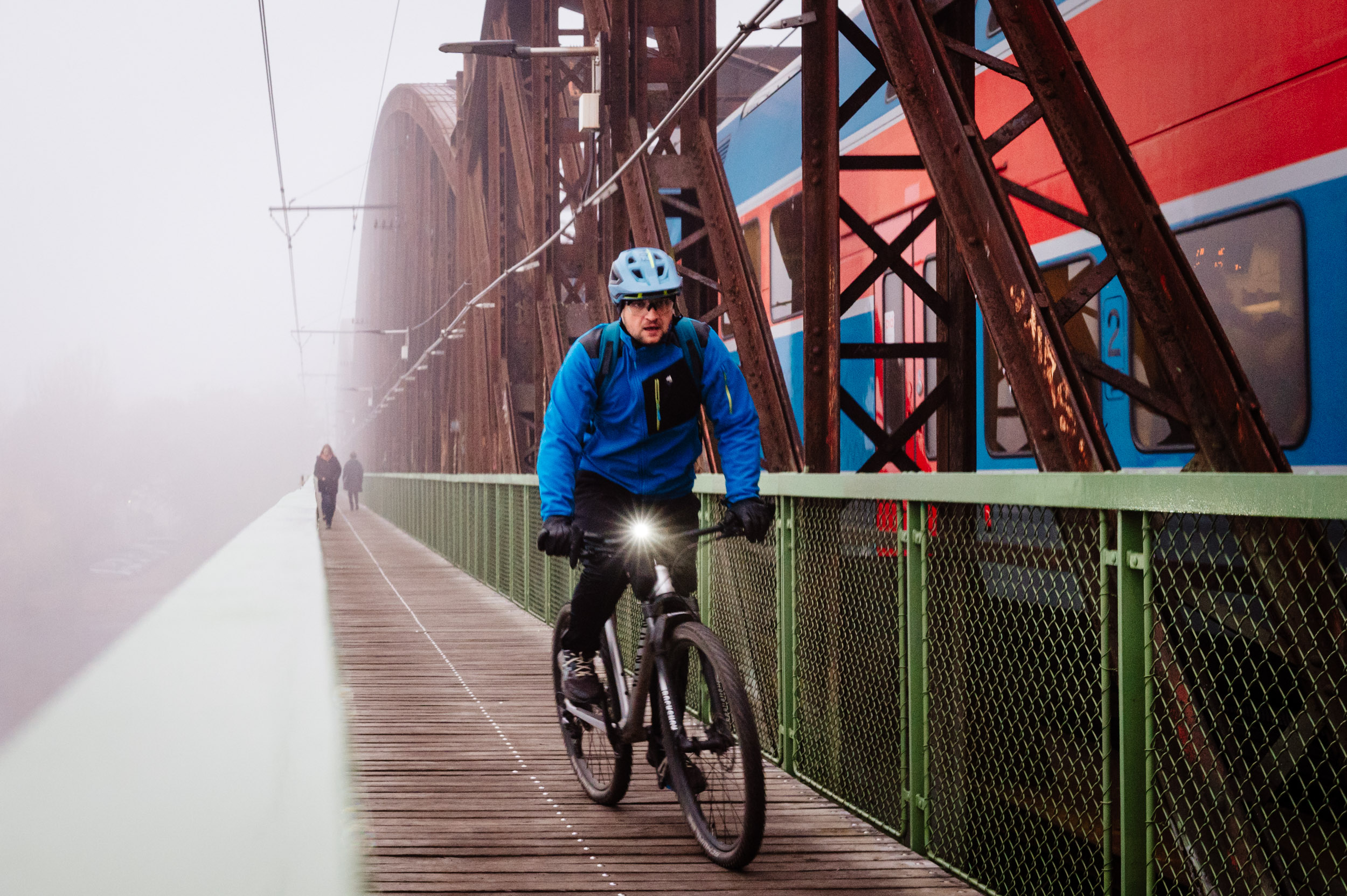 A guy on his bycicle coming down a train bridge in the foggy morning.