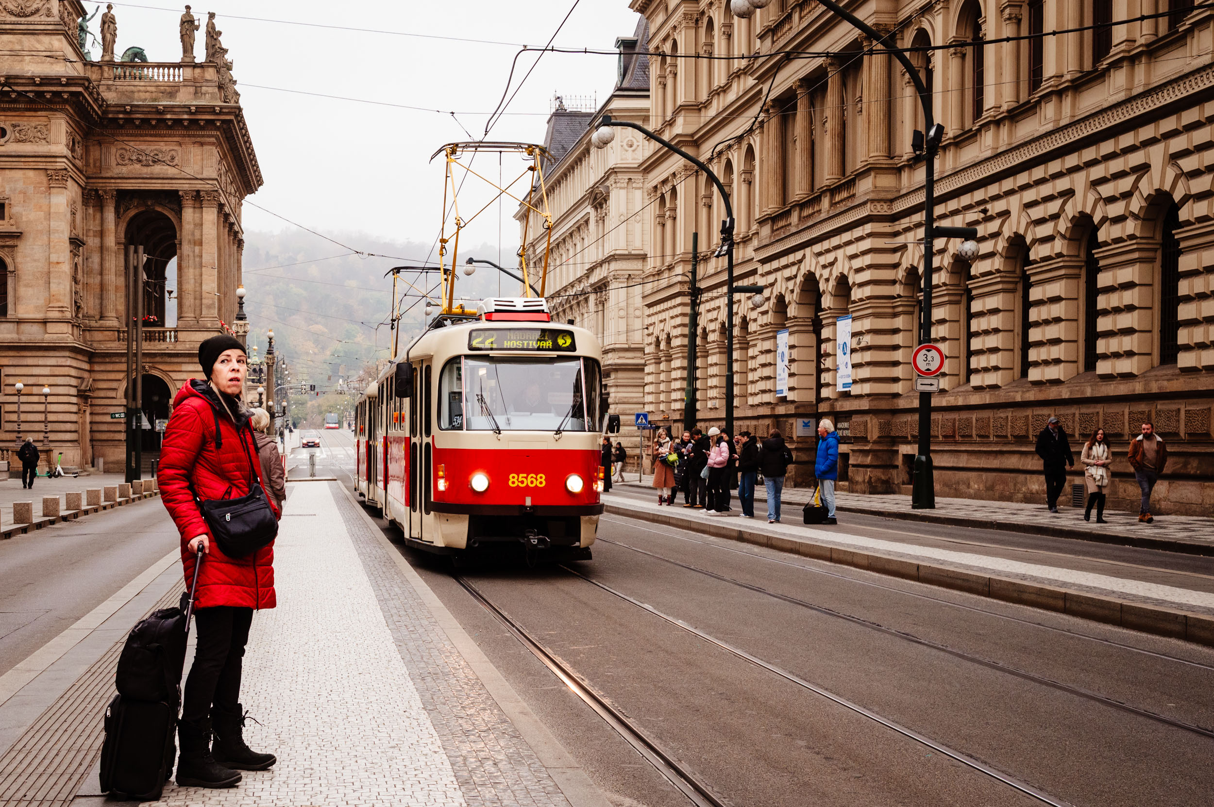 Woman in red coat waiting for the approaching tram in Prague.