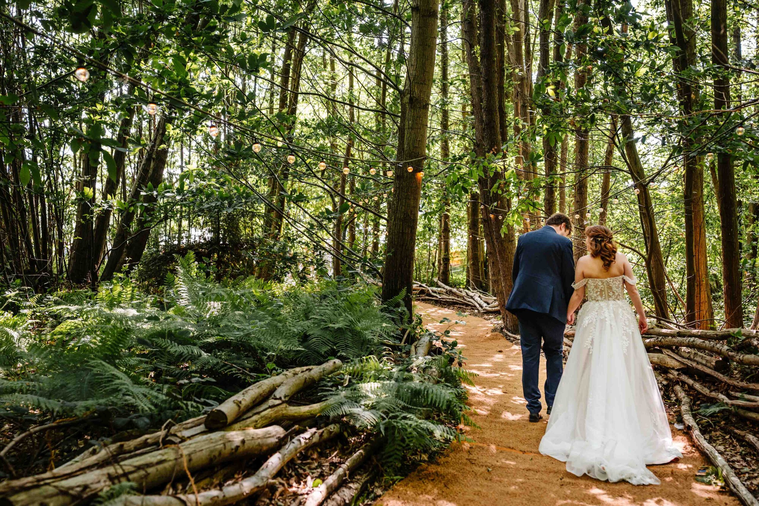 Bride and groom walking together through woodland paths at The Dreys wedding venue.