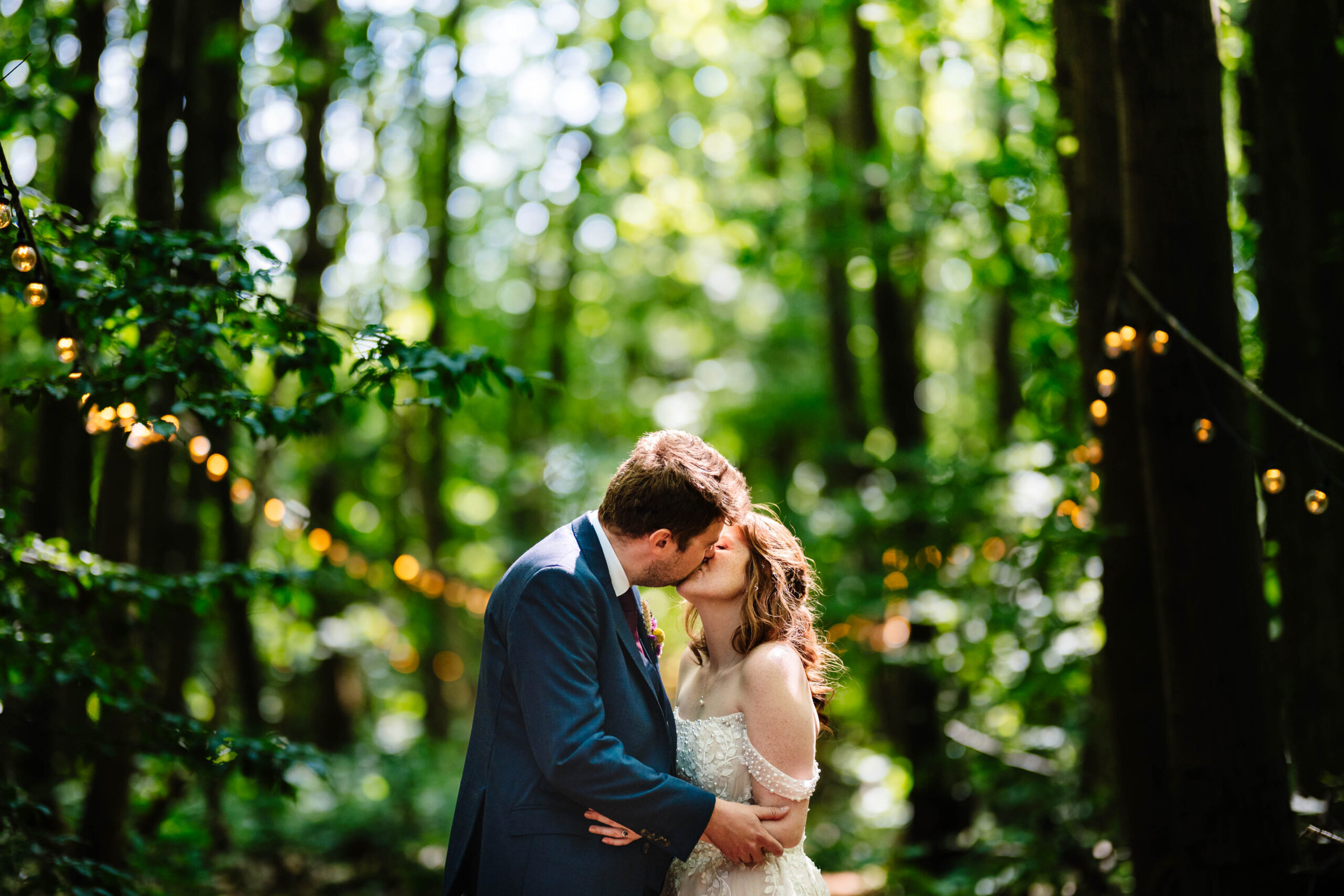 Bride and groom embracing beneath festoon lights during golden hour at The Dreys.