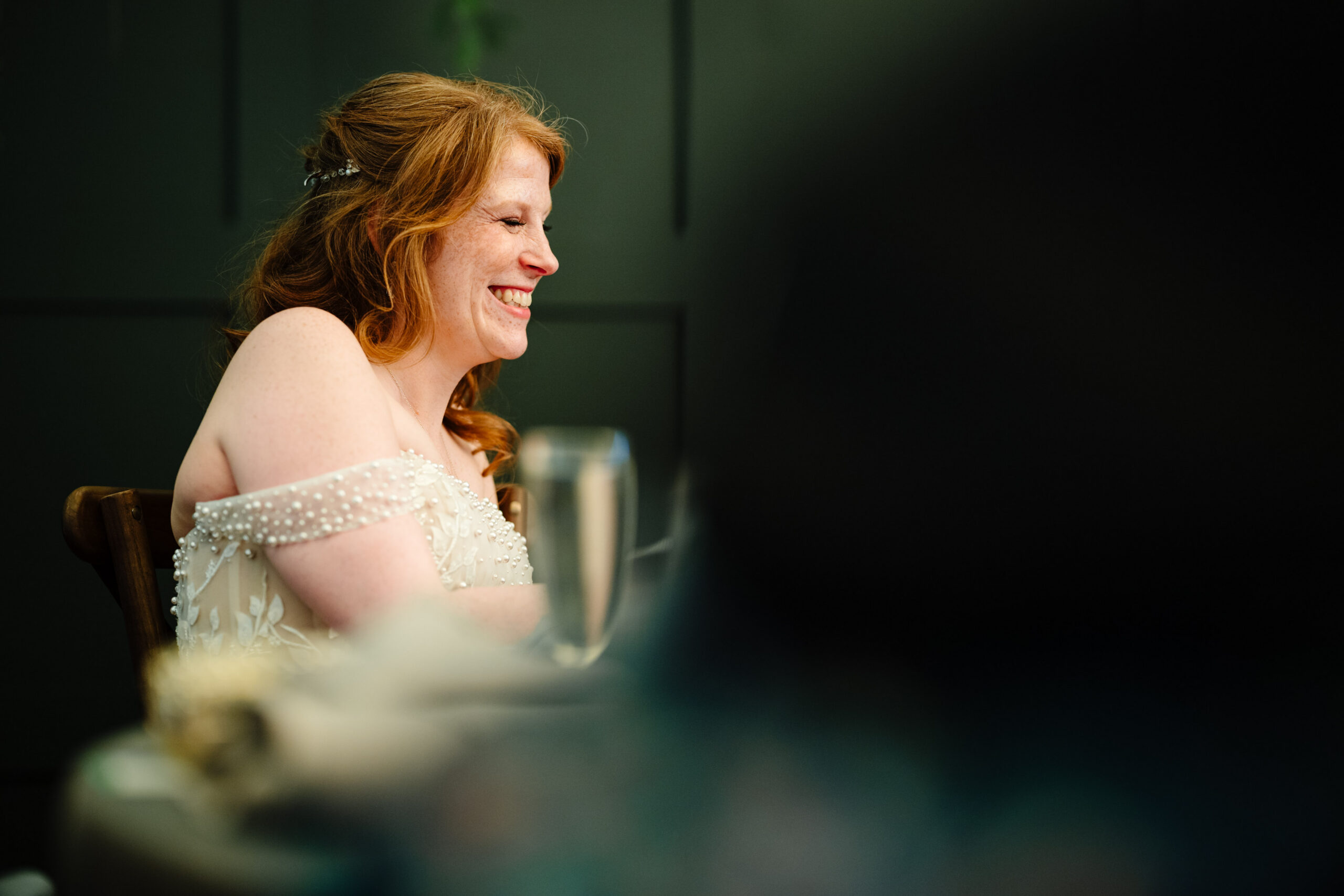 Bride smiling during speeches at her wedding reception in Kent.